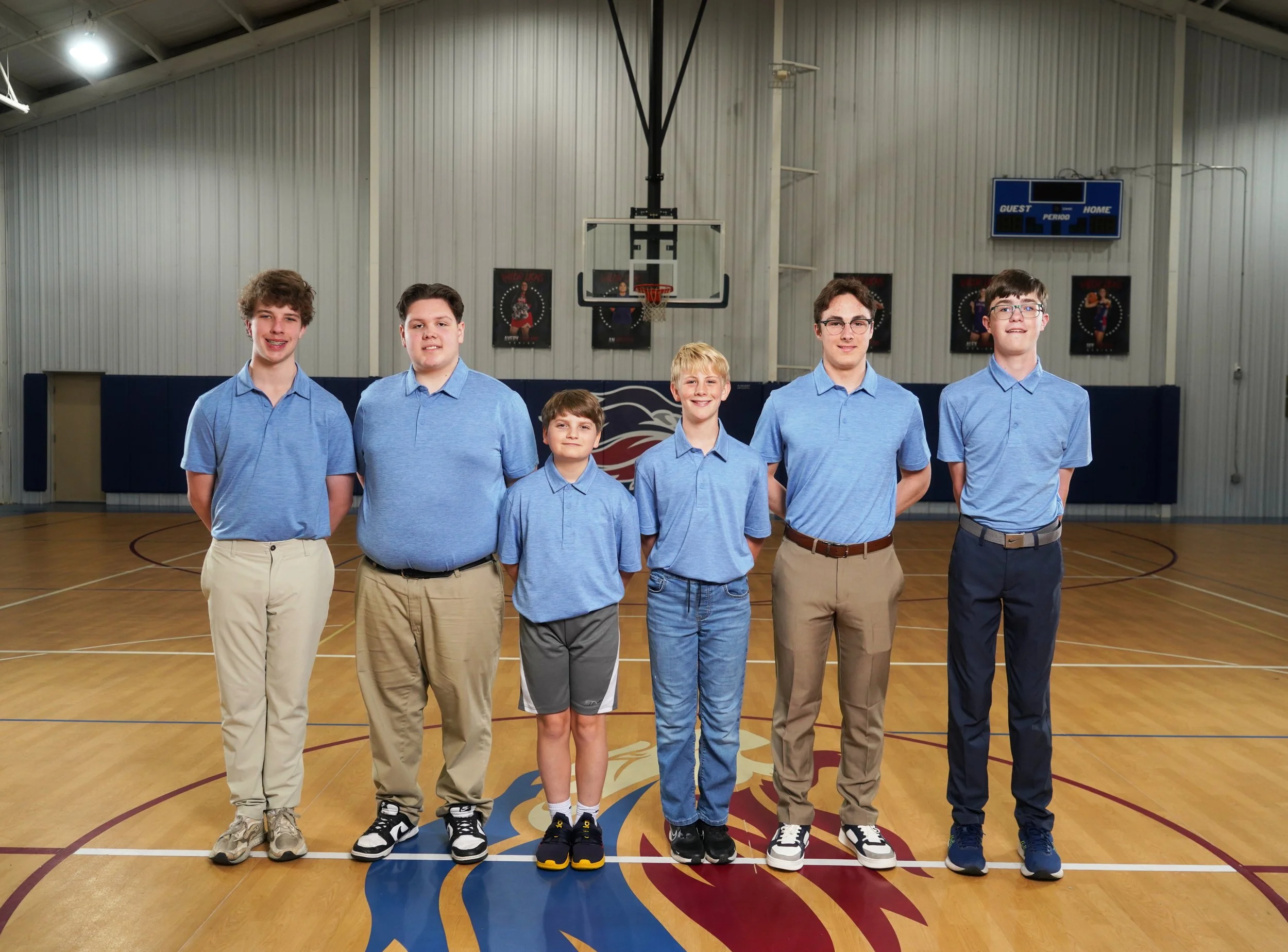Group of six young basketball players standing in a gymnasium, wearing matching red T-shirts with a lion logo and the words 'VALOR ATHLETICS' printed on them.