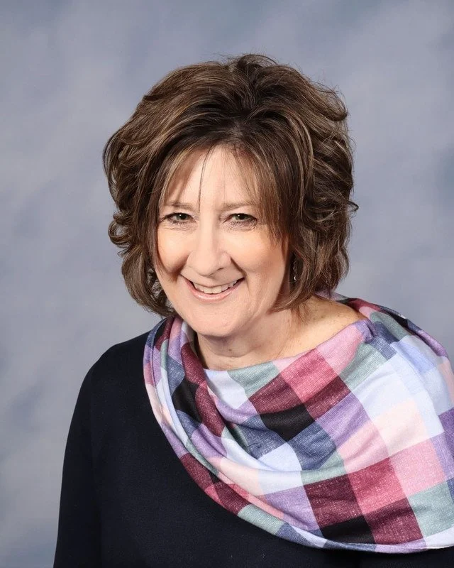 A shield-like emblem with a stylized rock climbing harness and tools in light blue on a dark blue background.