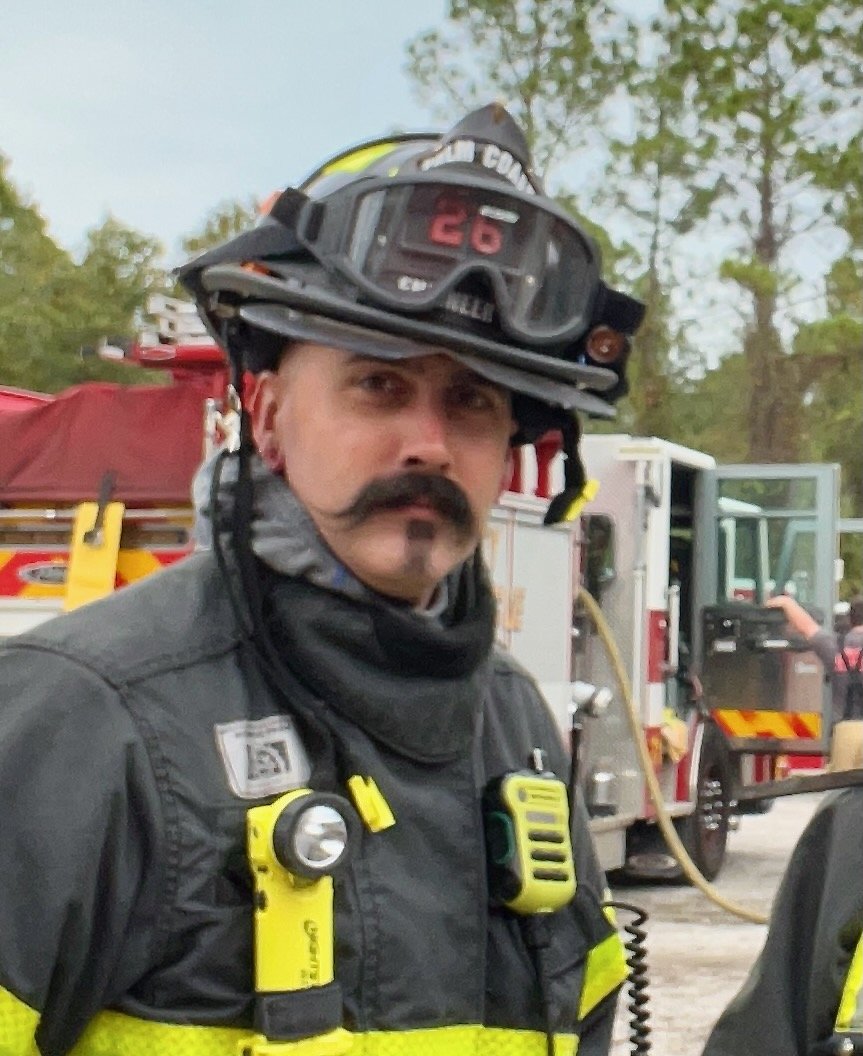 Firefighter wearing a helmet and protective gear beside a fire truck