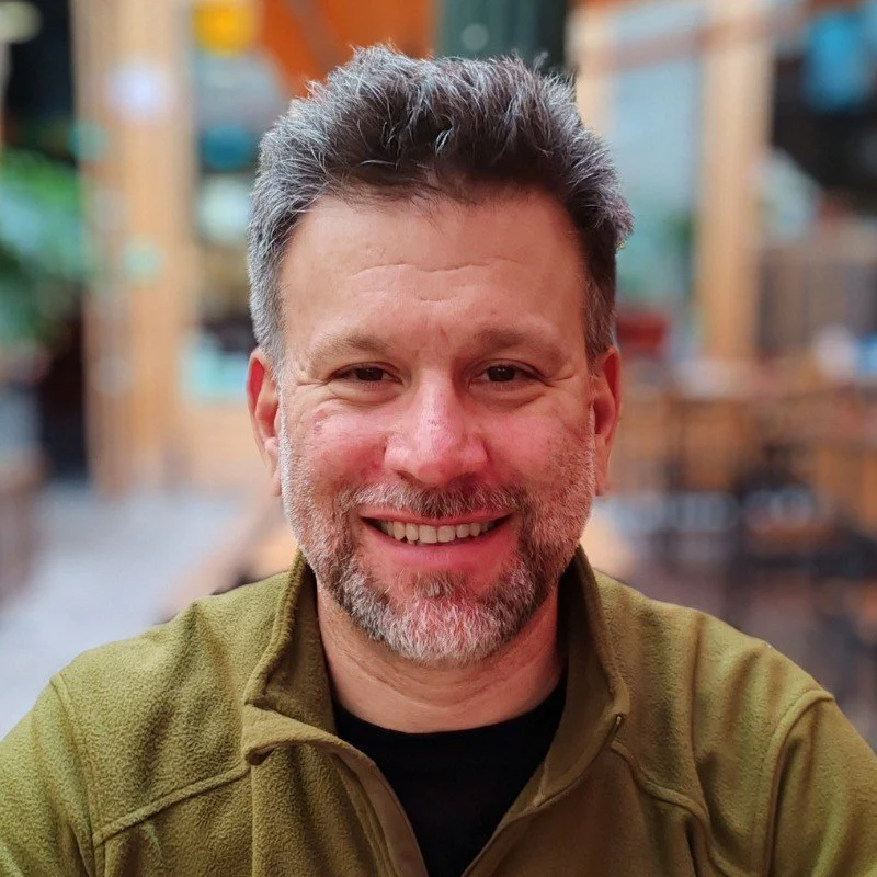 Persona sonriente en un entorno interior con fondo desenfocado.