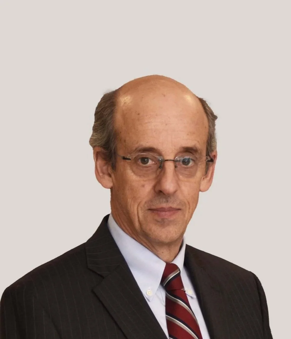 Hombre mayor con traje oscuro, corbata roja y gafas.