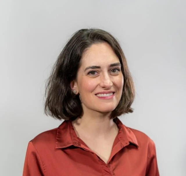 Retrato de una mujer con cabello corto y camisa roja, sonriendo, sobre un fondo neutro.