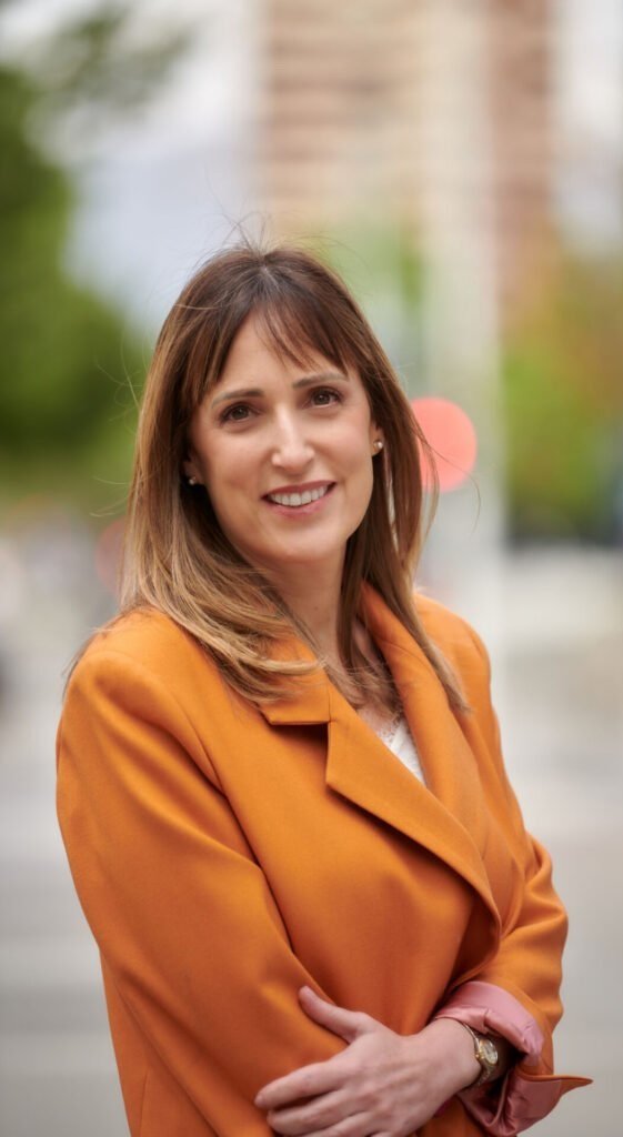 Mujer sonriendo con saco naranja en un entorno urbano.