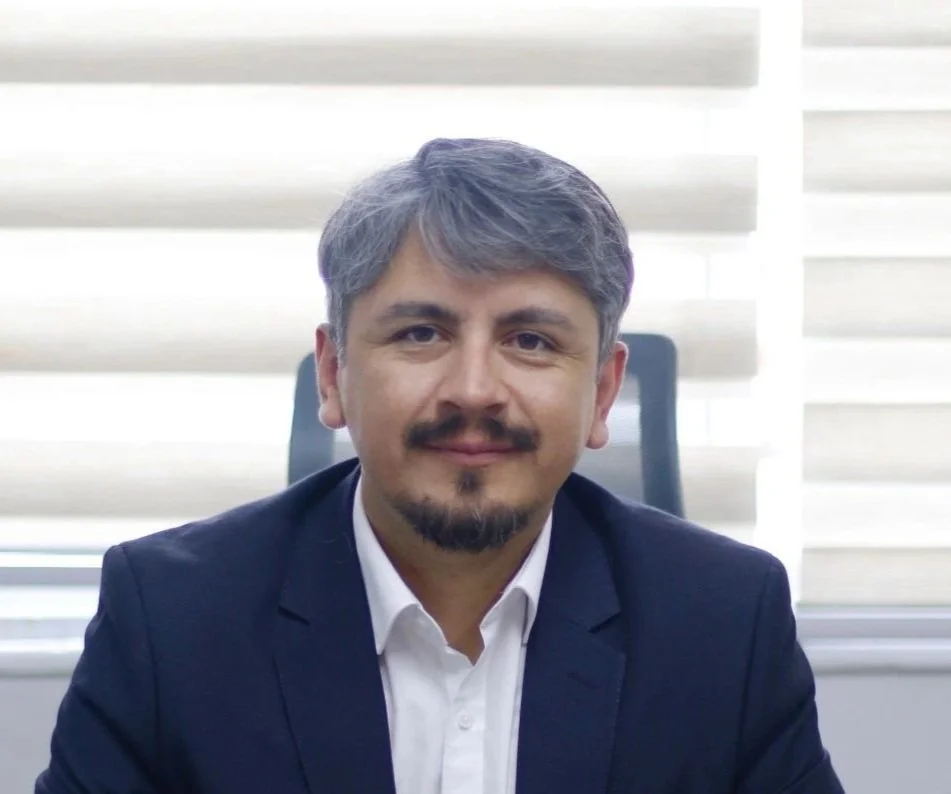 Hombre sonriendo en una oficina, vestido con traje y corbata.