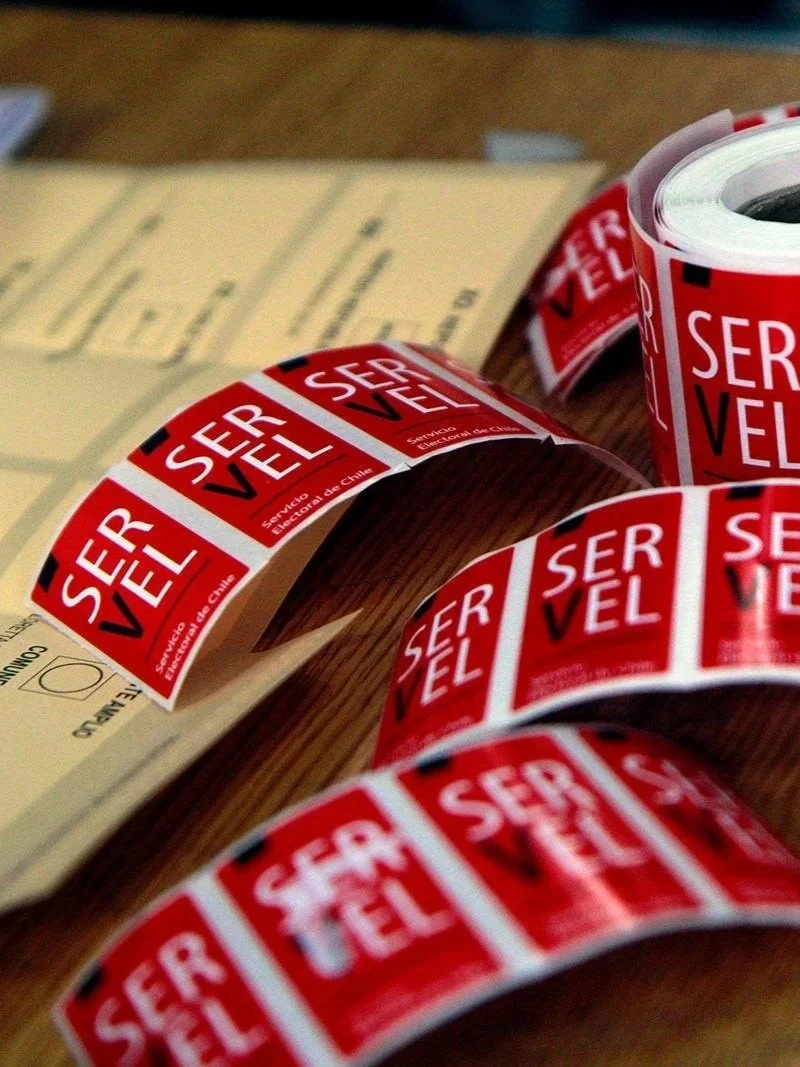 Etiquetas del Servel (Servicio Electoral de Chile) junto a una cédula de votación, material usado en las mesas electorales durante las elecciones en Chile