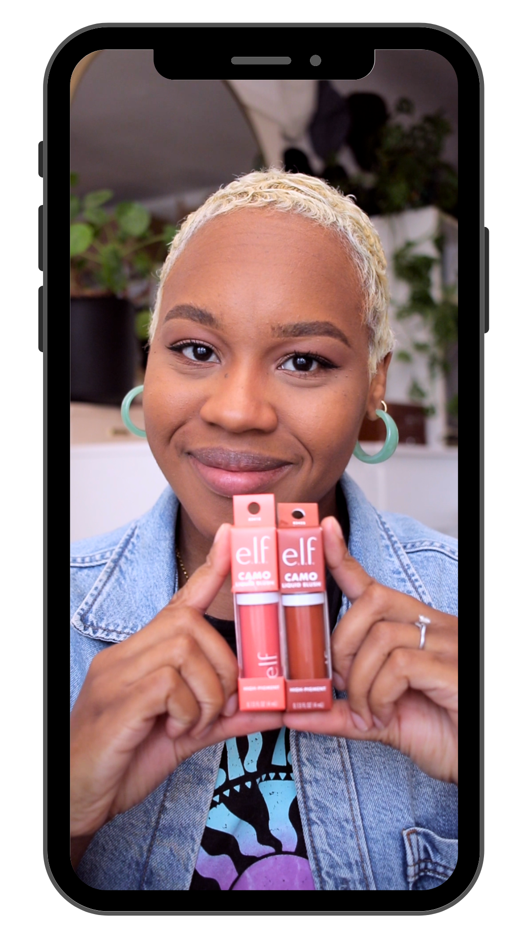 A woman with short blond hair and hoop earrings holding two ELF lip glosses, smiling at the camera.