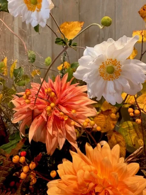 A colorful arrangement of flowers including white, pink, and orange blossoms with green and yellow accents, set against a background of a wooden fence.