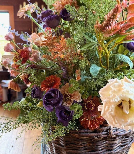 A colorful bouquet of various flowers in a wicker basket on a wooden table.