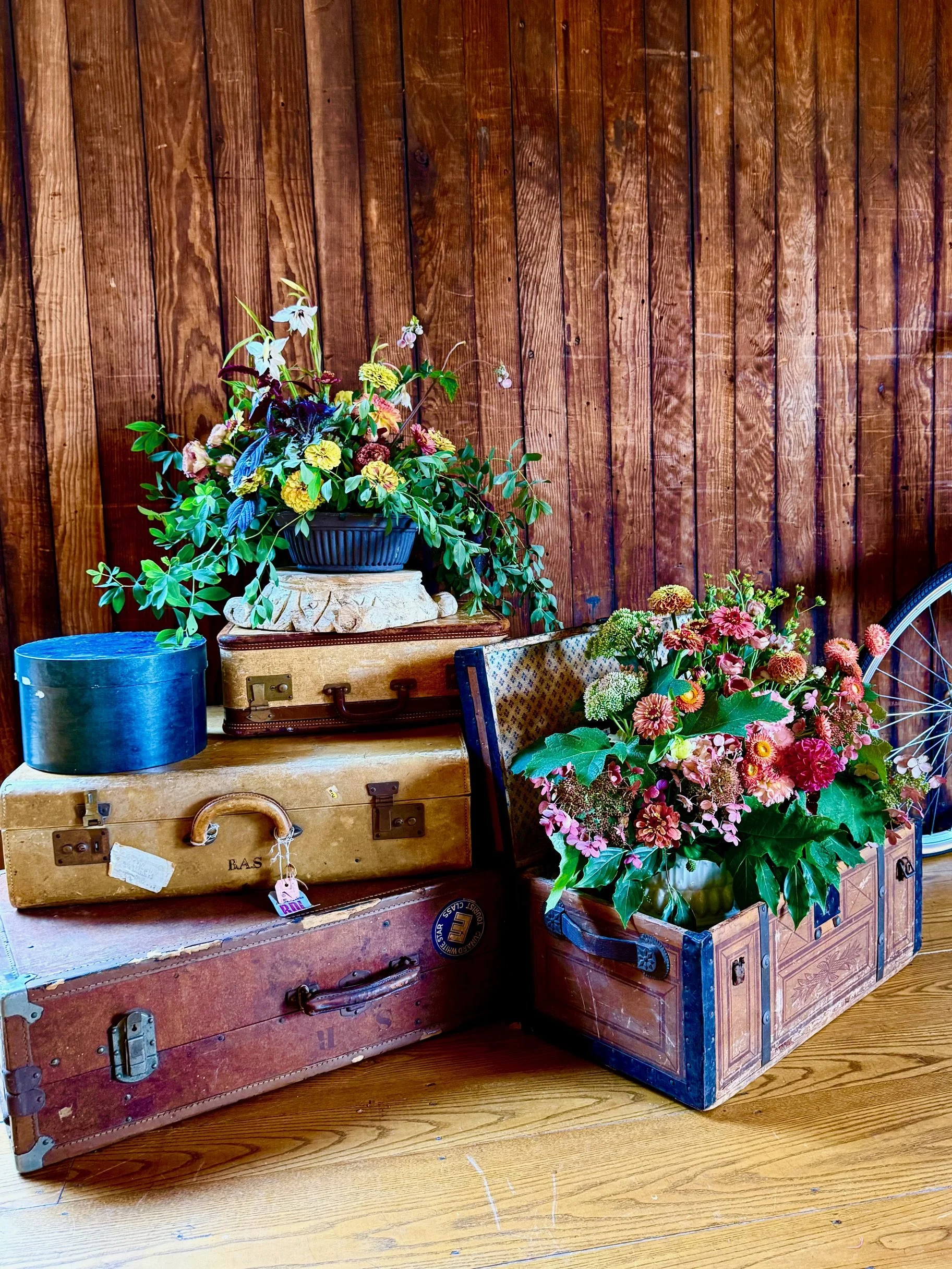 Vintage suitcases stacked with flower arrangements in a rustic setting.