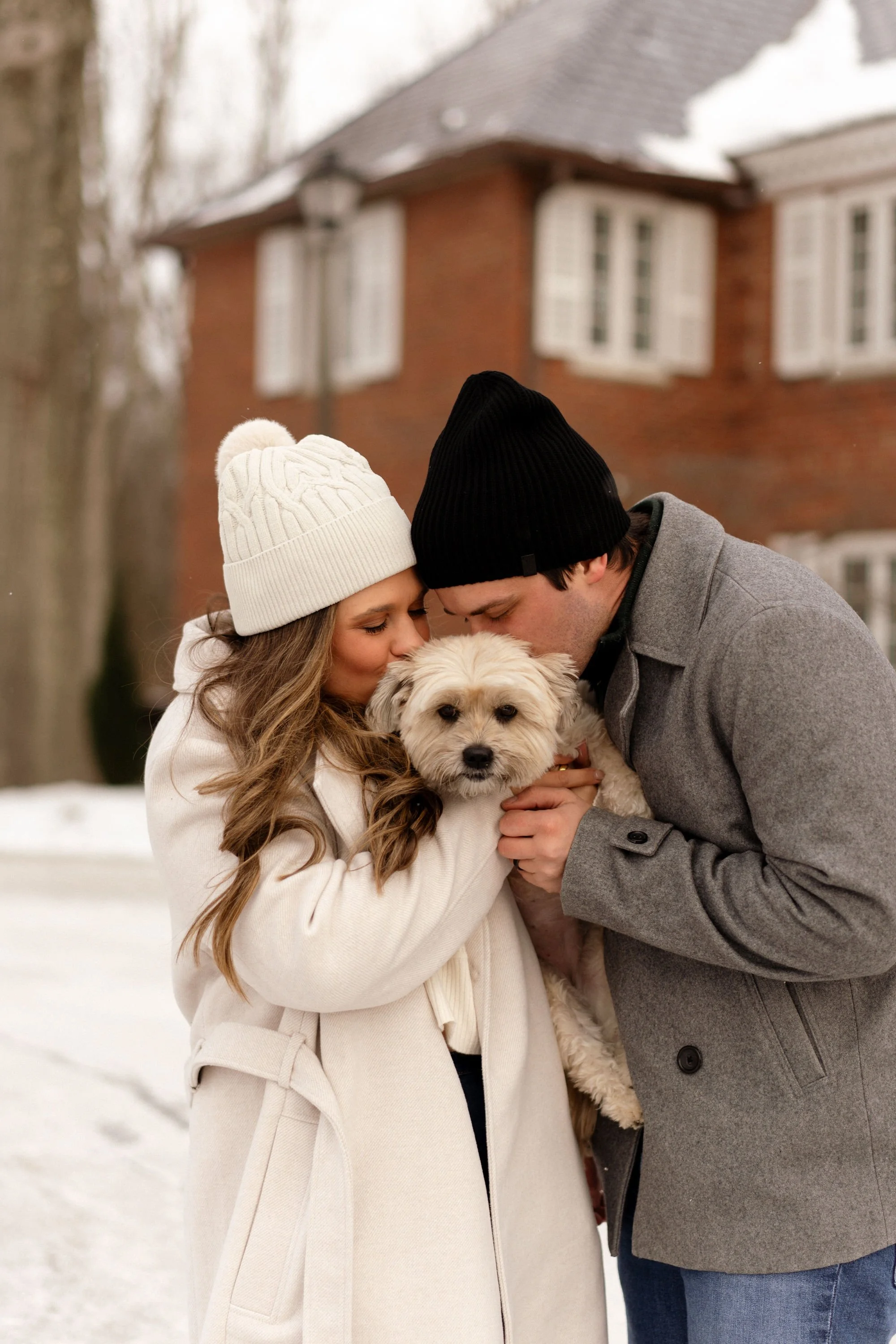 Young couple in winter clothing hugging their dog outside on a snowy day.