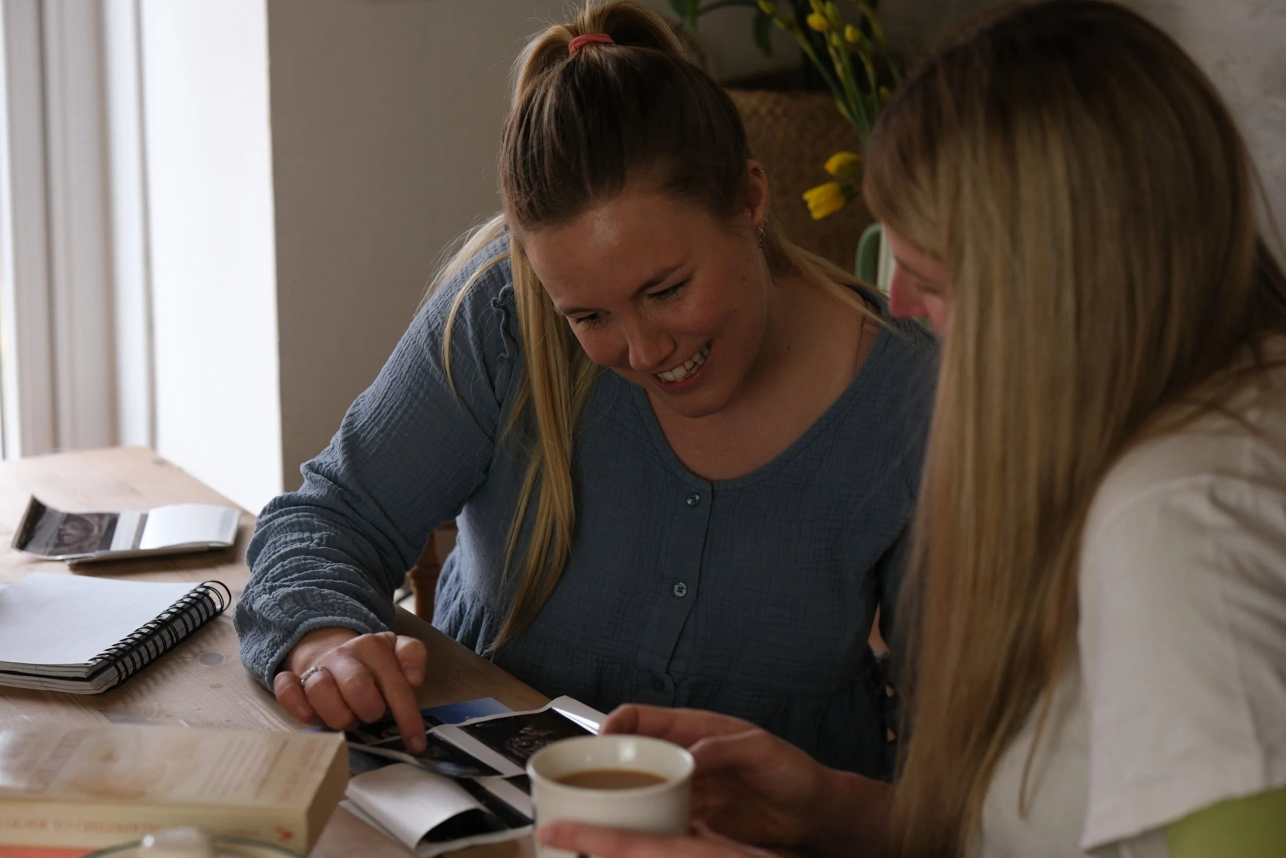 A pregnant mum sits in her home with her private independent midwife Katie. They are looking at ultrasound scan photos and discussing pregnancy care, NIPT testing, hypnobirthing and pregnancy massage.