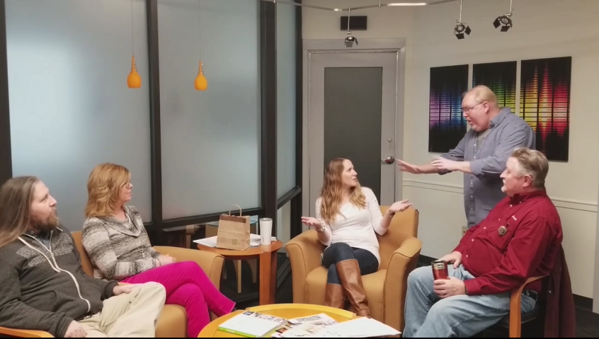 Five co-workers discuss ideas in a breakroom.