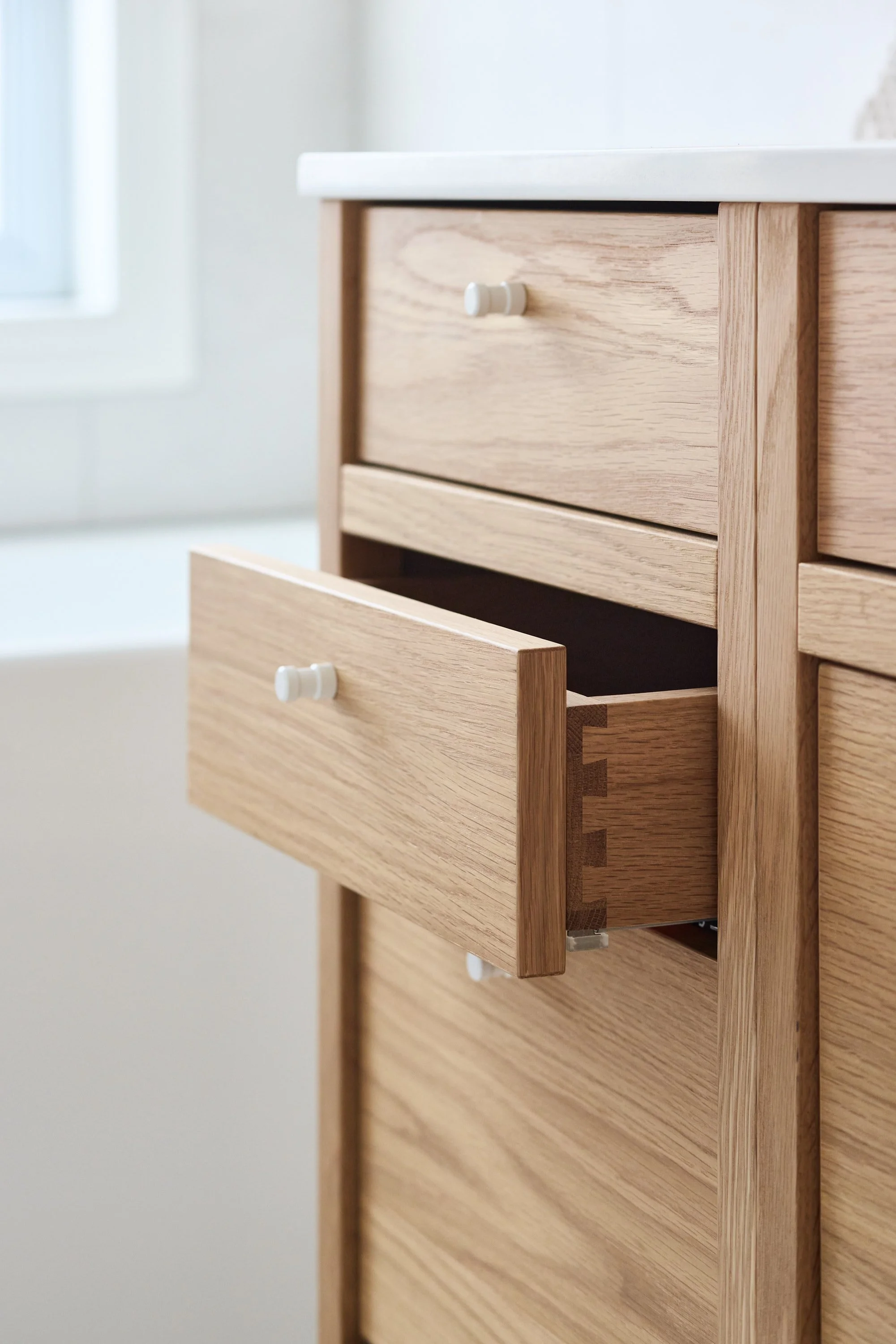 Salle de bain moderne avec vanité modulaire freestanding en chêne naturel, assemblage à queues d’aronde, lavabo blanc, et robinet chromé. Design épuré et matériaux naturels.