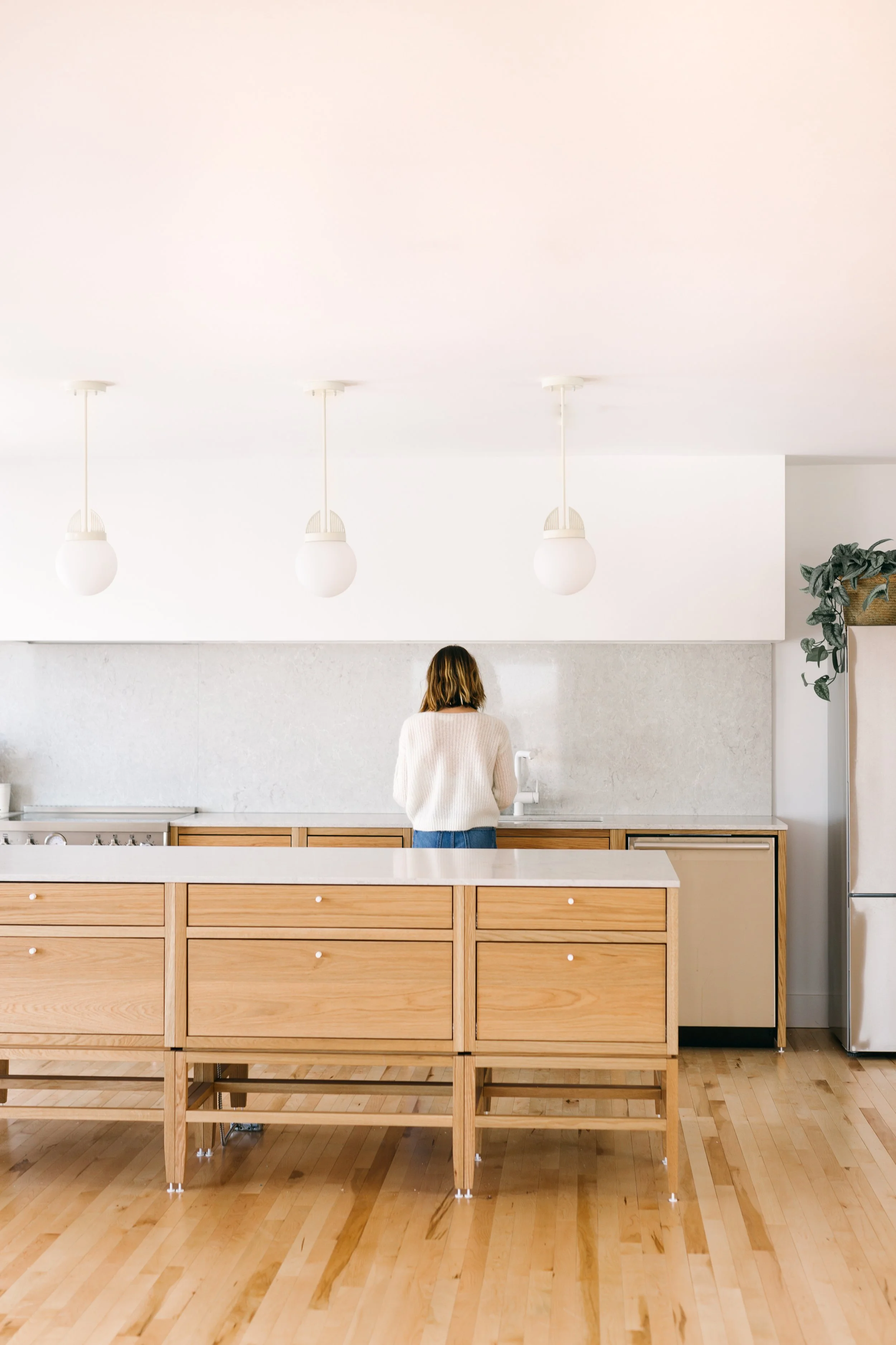 Cuisine modulaire en chêne sur pattes avec grand îlot surélevé, comptoir et dosseret en quartz gris, électros inox, hotte encastrée.