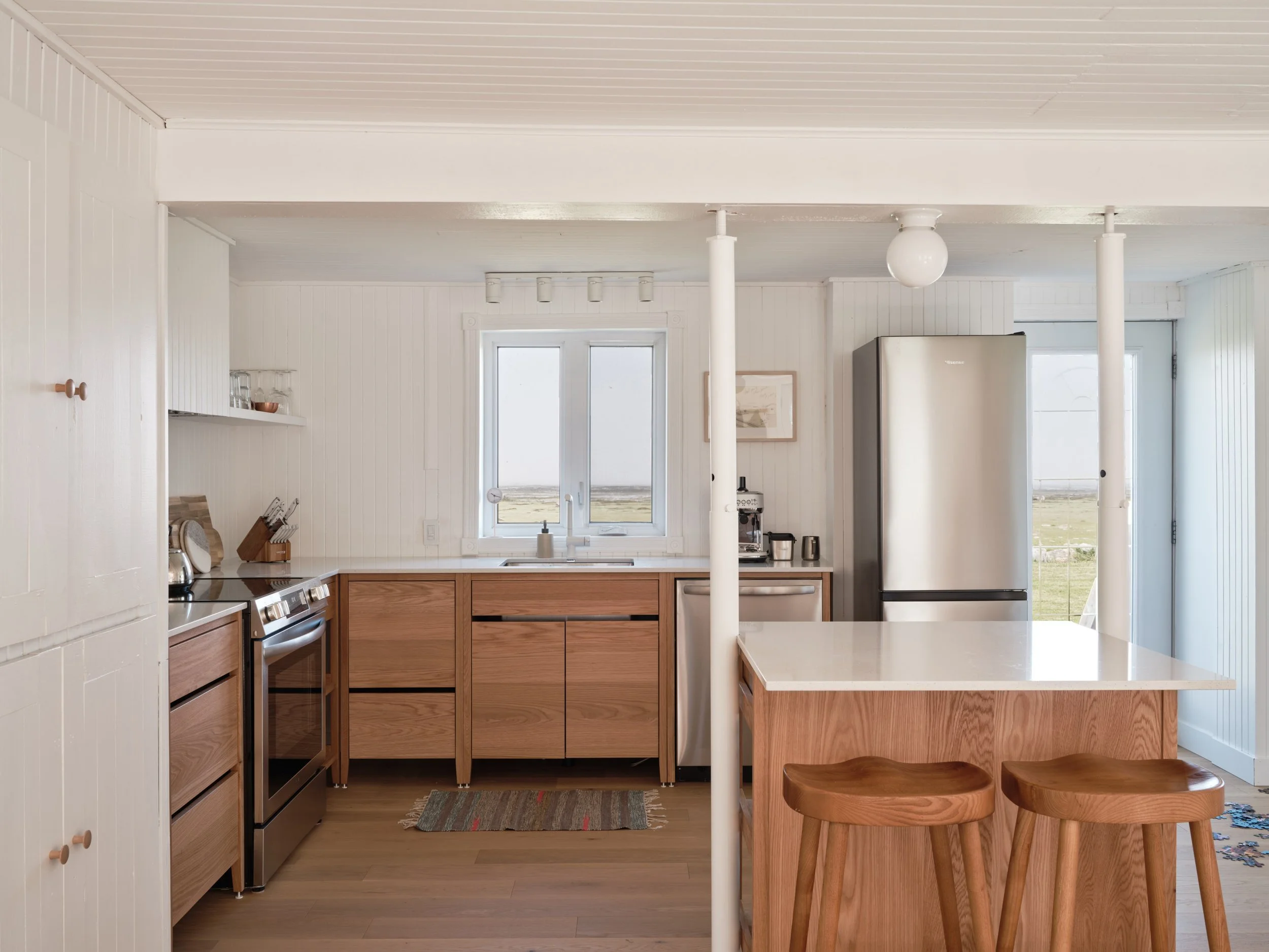 Cuisine Coquo en chêne naturel avec mini îlot et deux places assises, modules sur pattes, comptoir en quartz blanc, vue extérieure du fleuve et ciel magnifique.