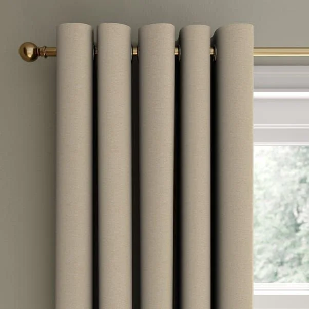 A set of five beige curtains hanging on a gold curtain rod with a decorative finial, partially covering a window with a view of trees outside.
