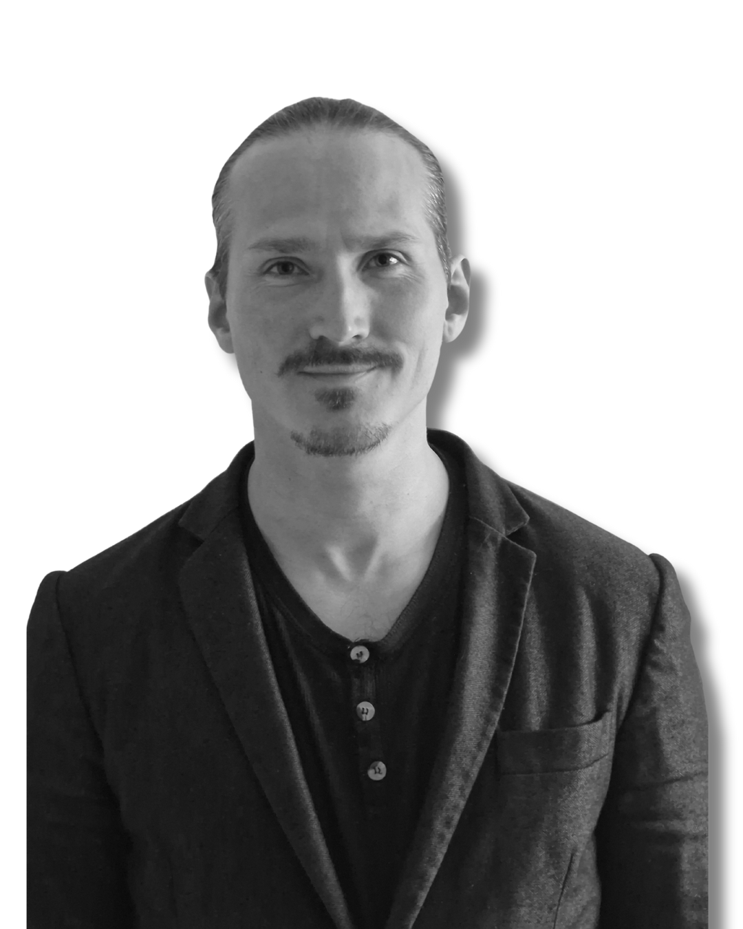Svartvit bild av en man med axellångt hår, lätt skäggstubb, iklädd svart tröja och mörk blazer, ser glad ut.
