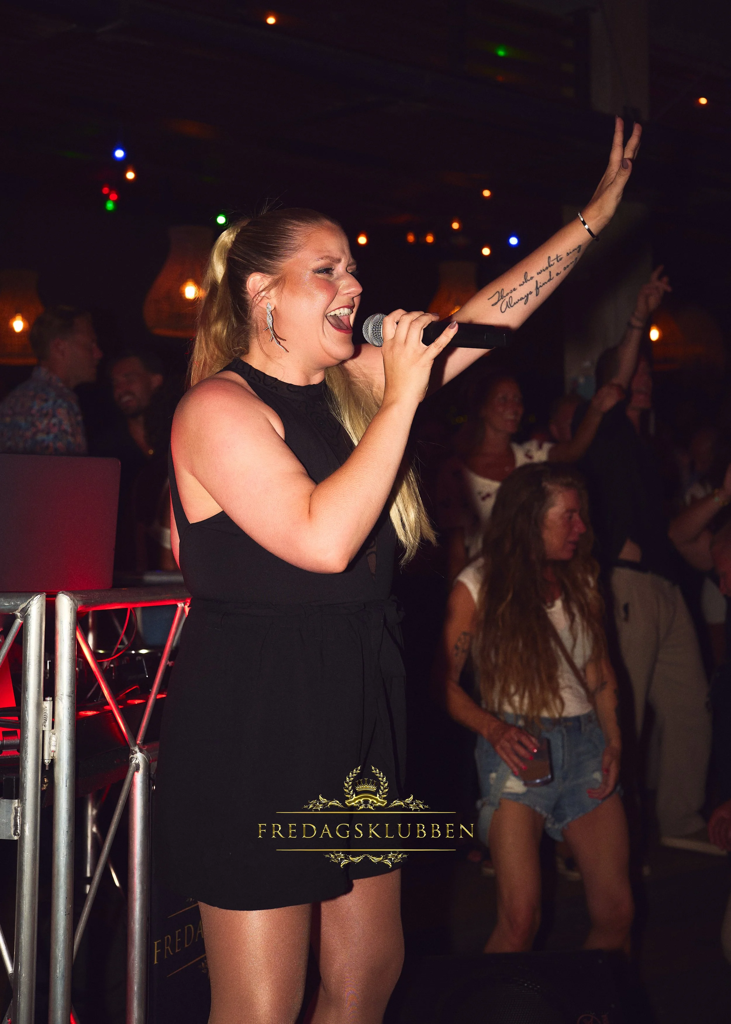 En kvinna sjunger och dansar på en nattklubb, omgiven av publik.
