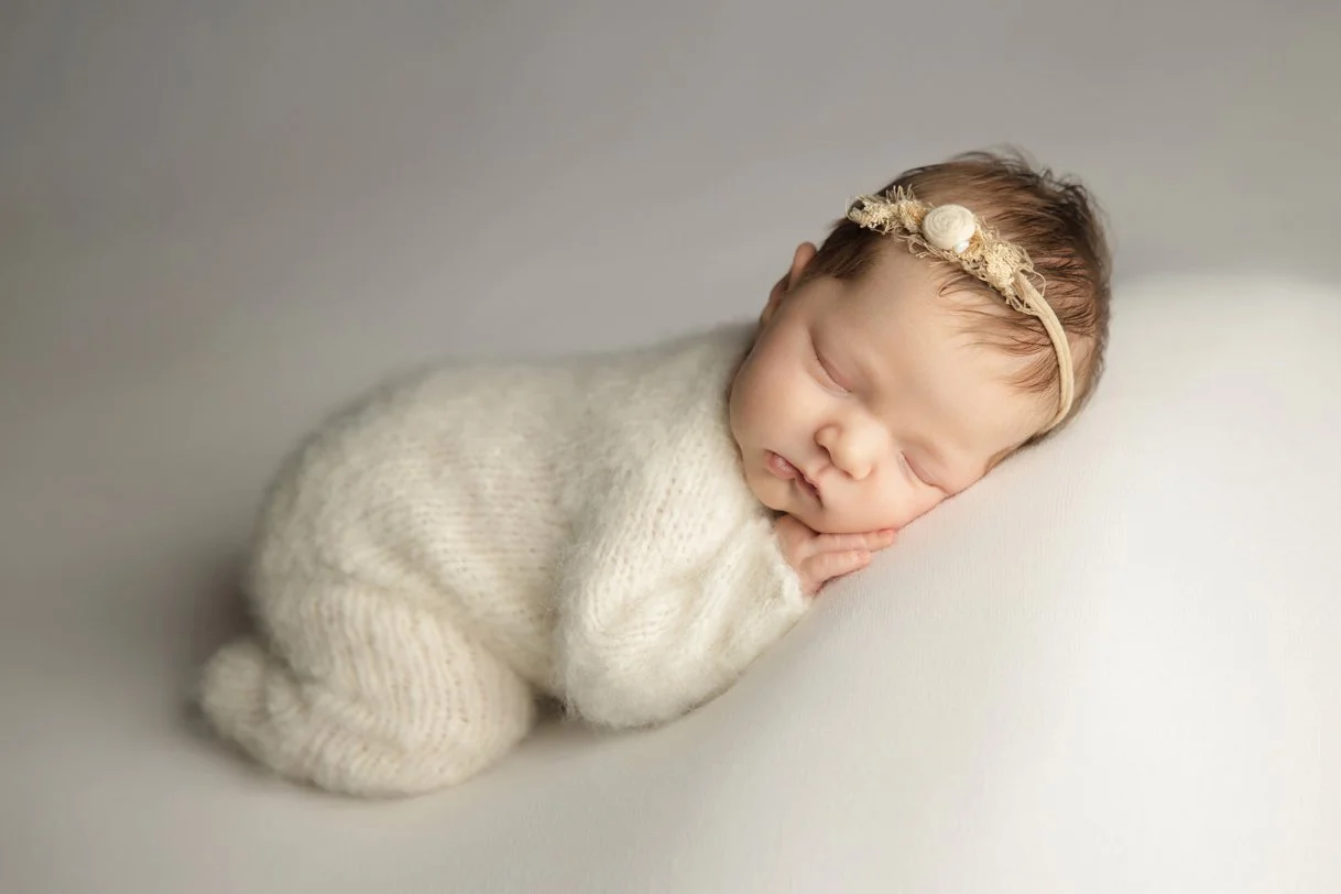 Newborn photograph by Andria Fontenot Photography of a baby on a cream blanket wearing a cream knitted romper