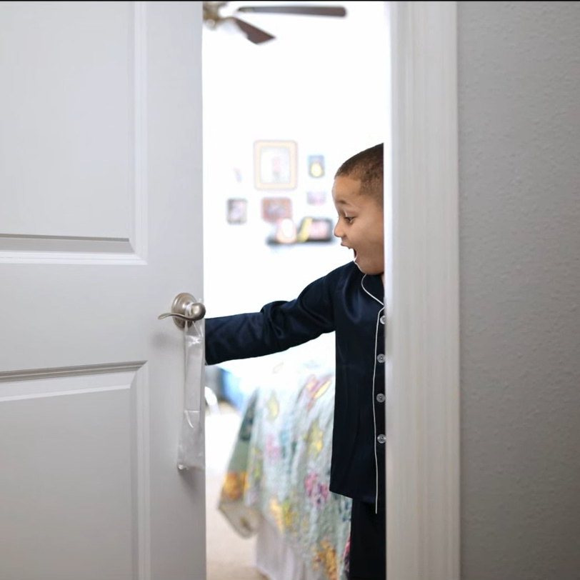 Young boy in pajamas opening a door with a surprised or excited expression in a bedroom with the tooth fairy bag hanging on the door handle.