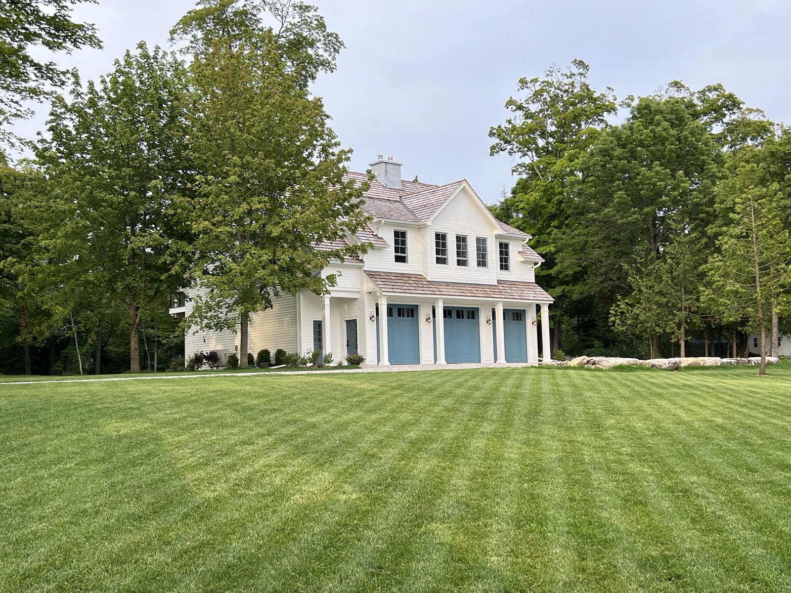 Large white house with blue garage doors surrounded by green lawn and trees.