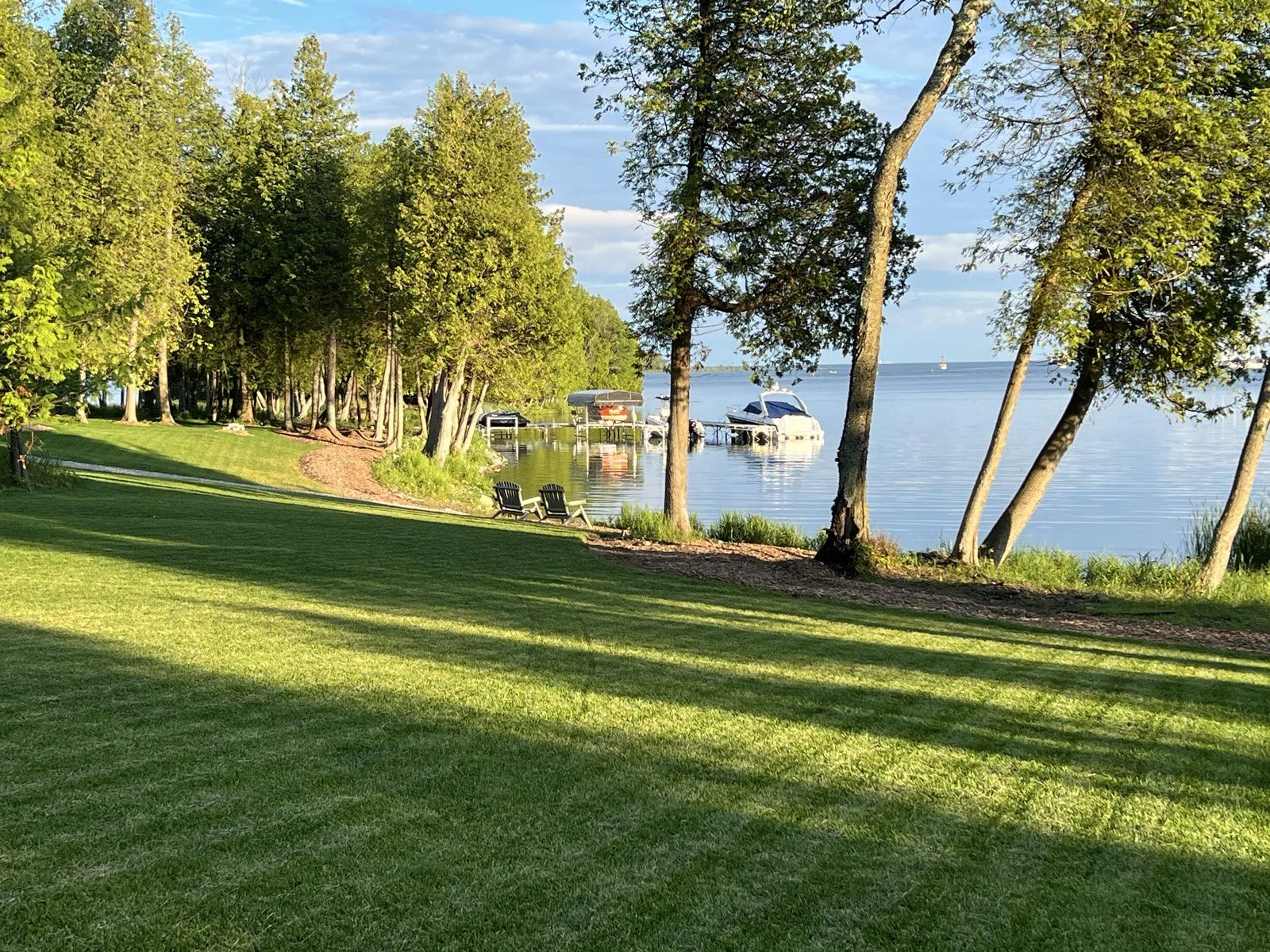 Lakeside view with trees, grass, and boats on a calm lake.