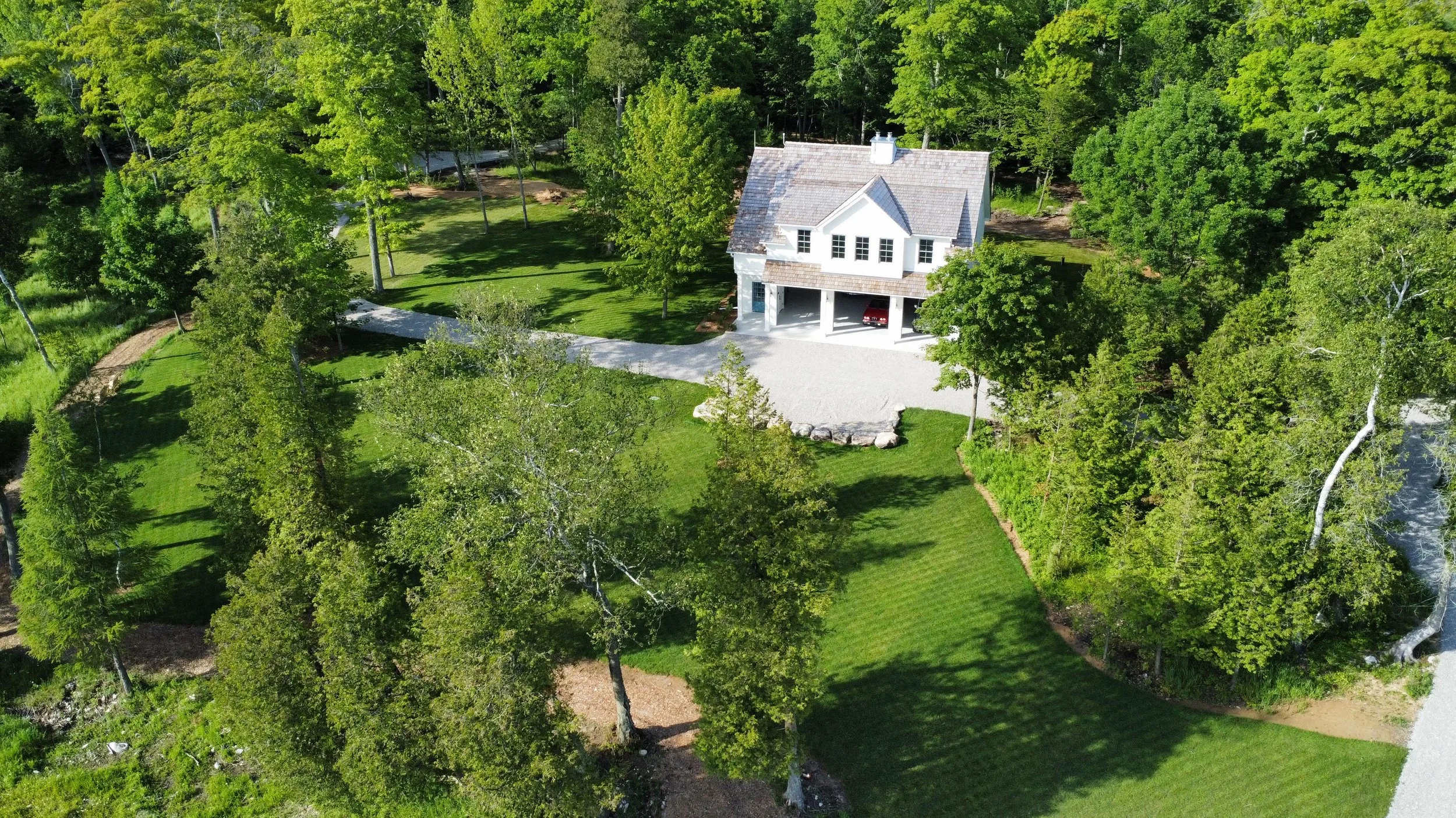 Aerial view of a white two-story house surrounded by a large green lawn and trees.