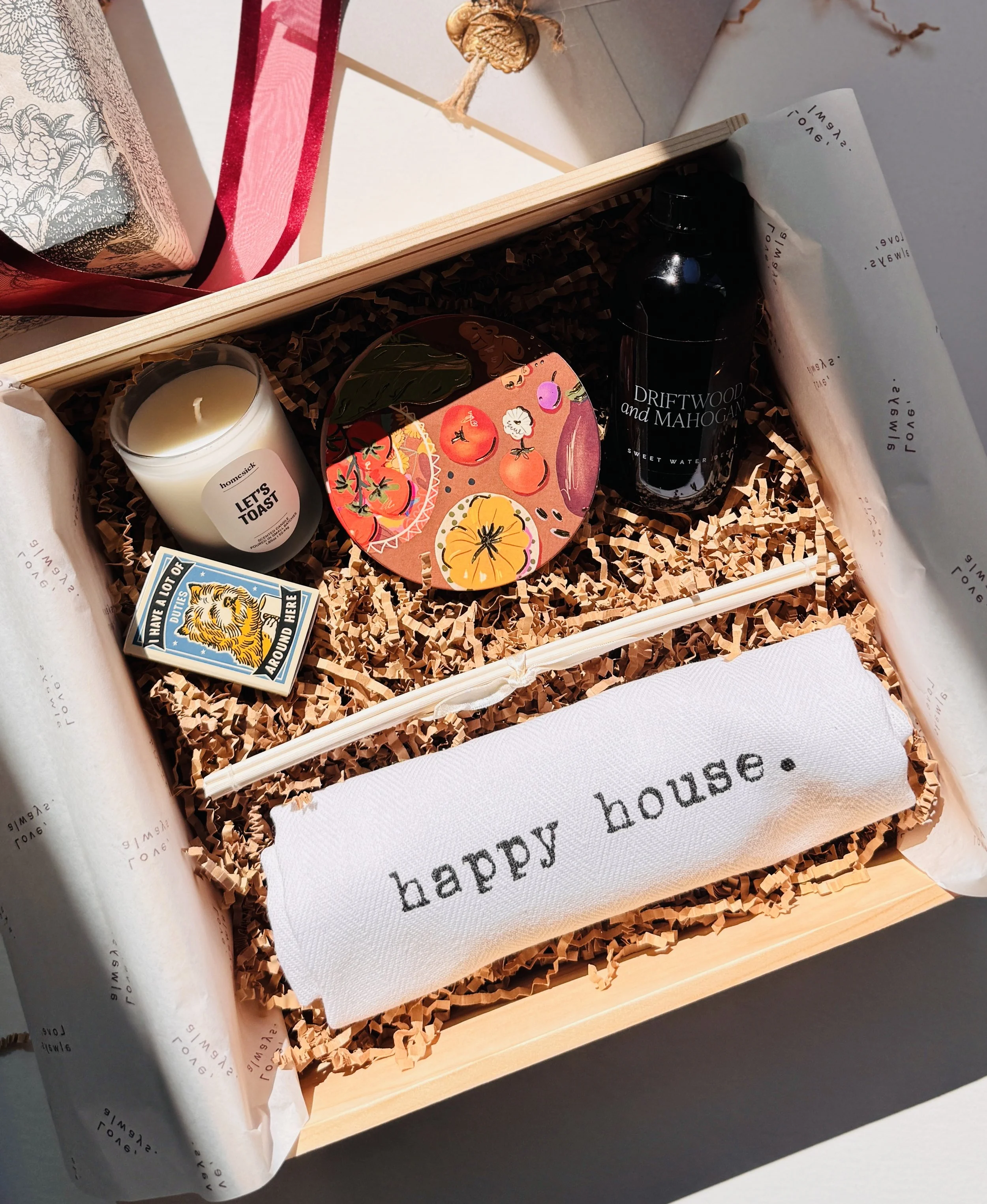 Luxury housewarming gift box with candle, diffuser, hand-painted coaster, matchbox, and embroidered “happy house” kitchen towel in a pine-wood box.