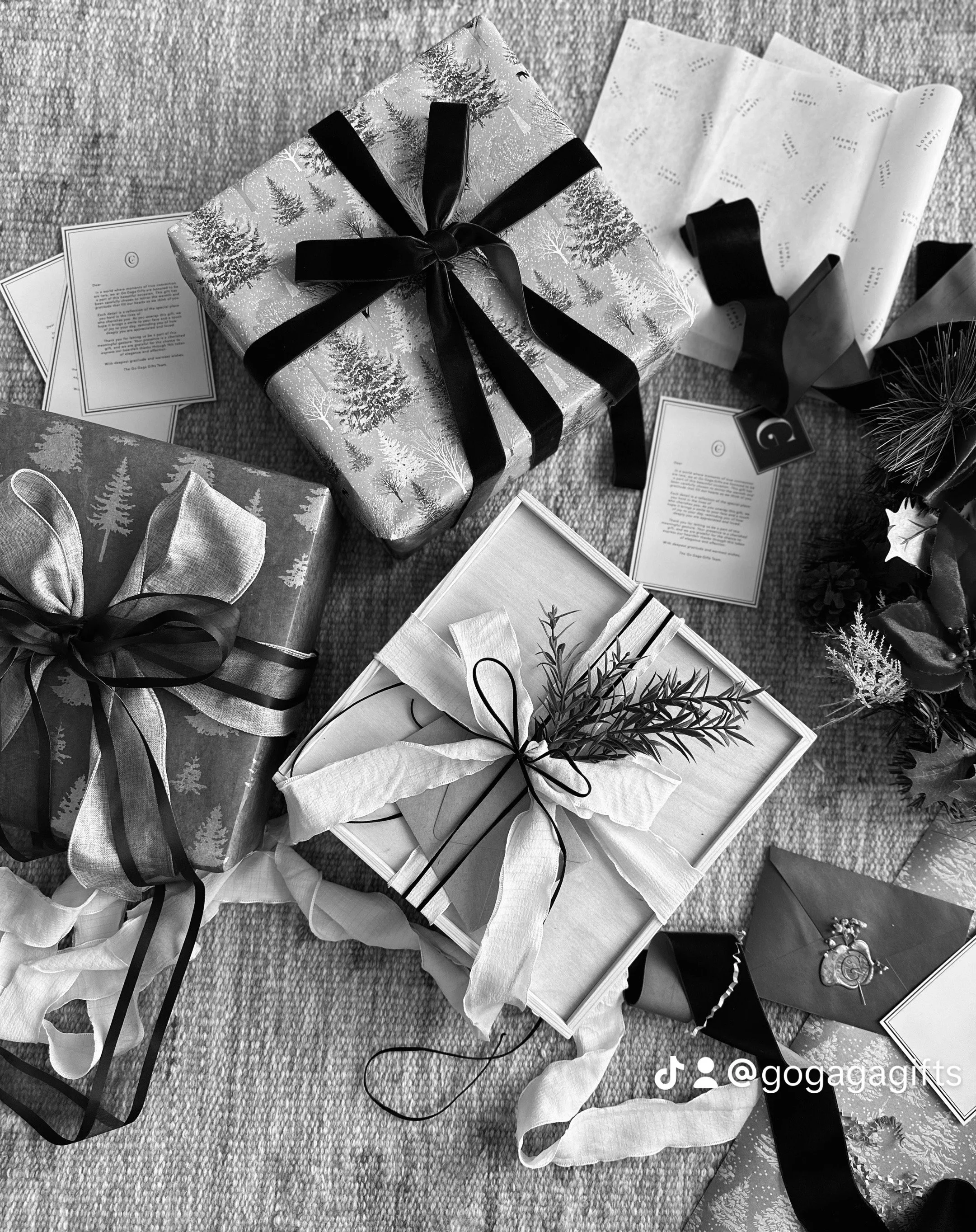 Black and white photo of wrapped Christmas presents with ribbons and decorative tags, placed on a textured surface.