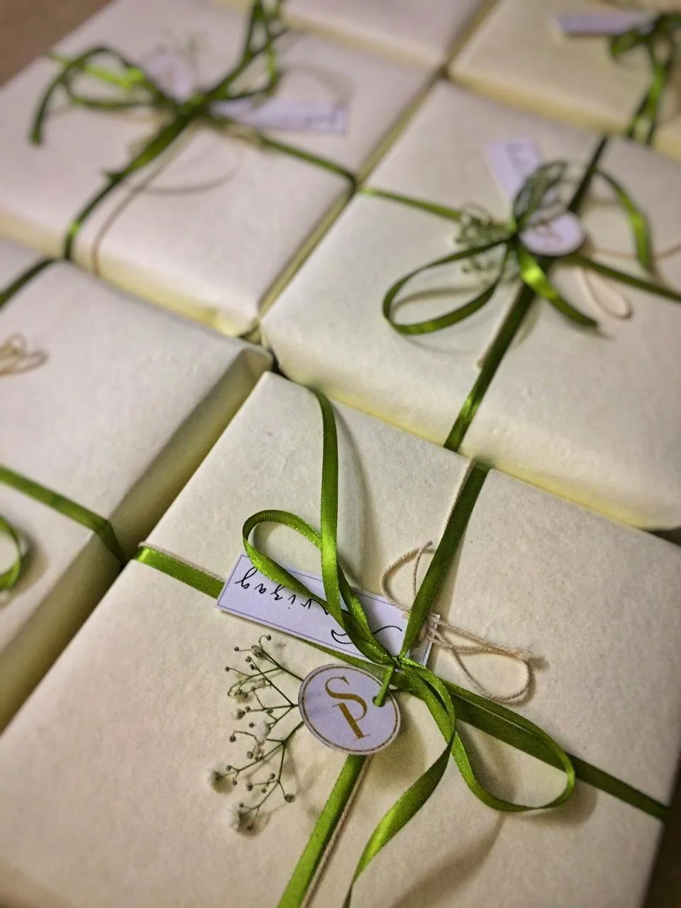 Cream-colored gift boxes wrapped with green ribbons, decorated with small white tags and sprigs of baby's breath flowers.