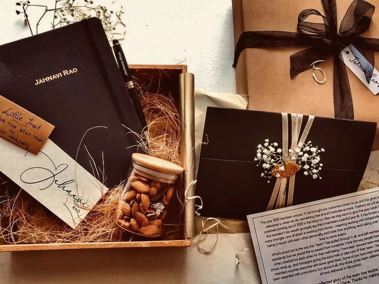 A gift box with black and white cards, a jar of almonds, and a wrapped gift with a black ribbon.