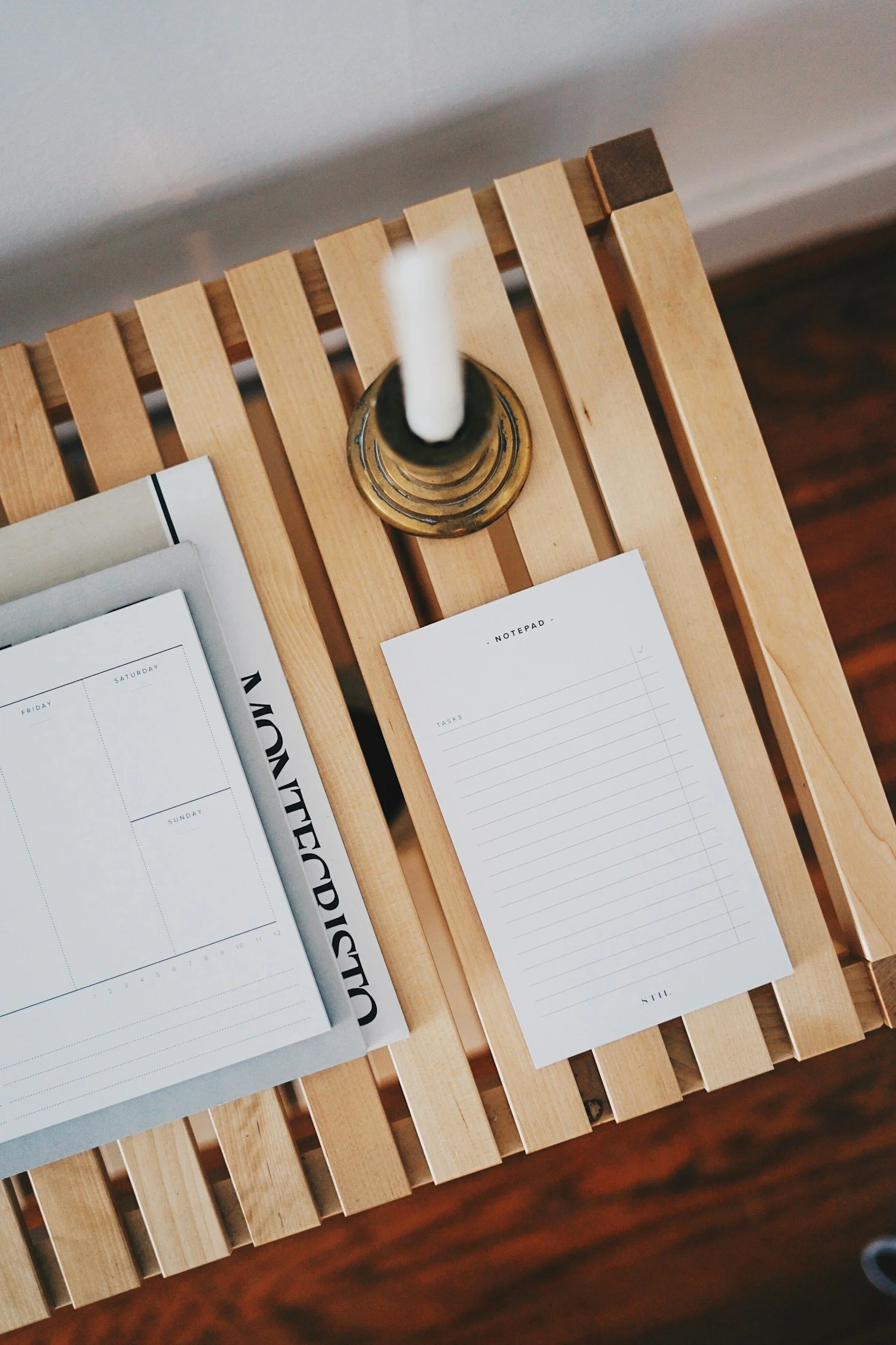 Top view of a wooden bench with a candle and open planner on it.