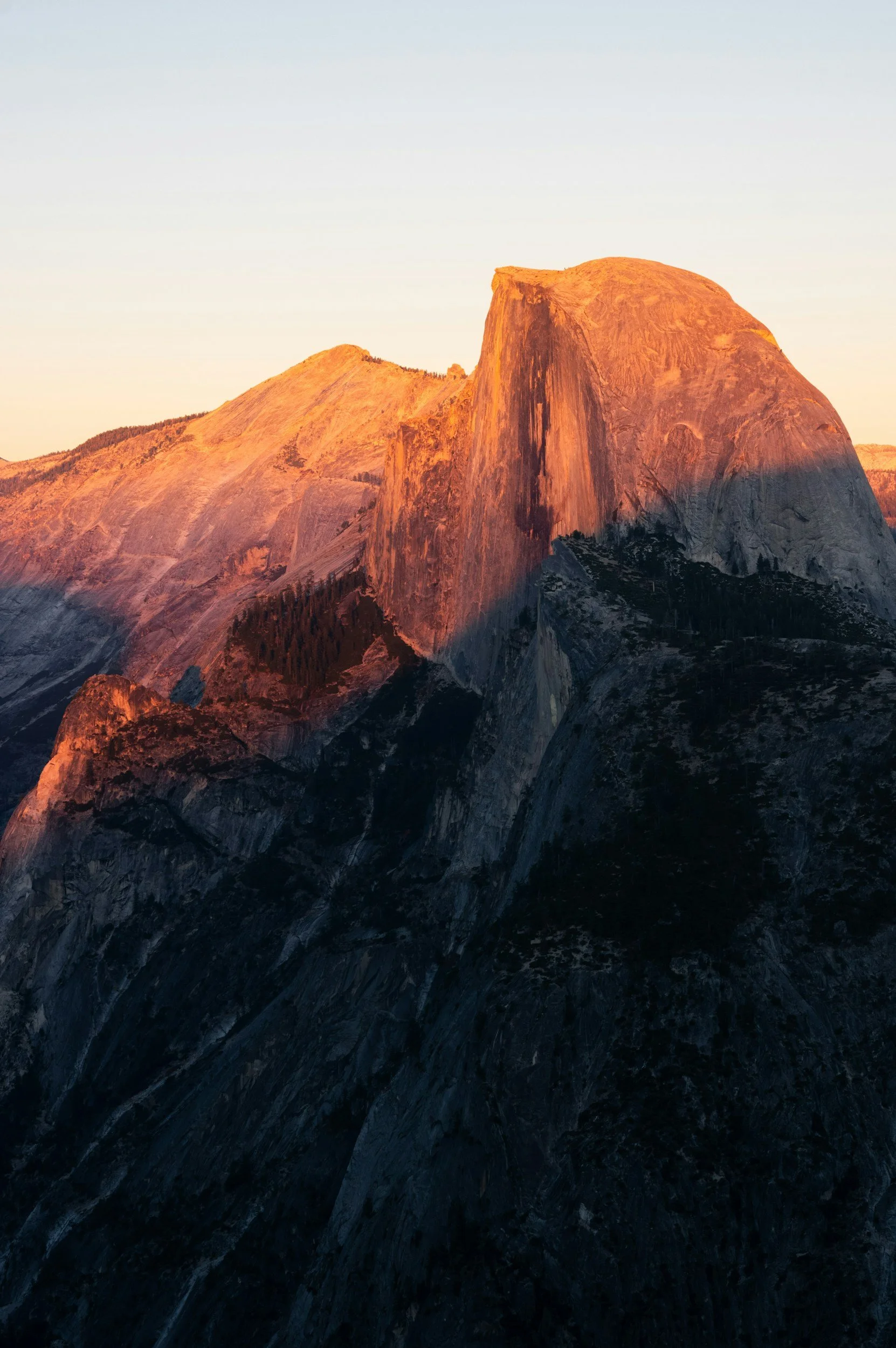 Sunset over a mountain with a large, prominent granite formation, casting shadows on the rugged terrain.
