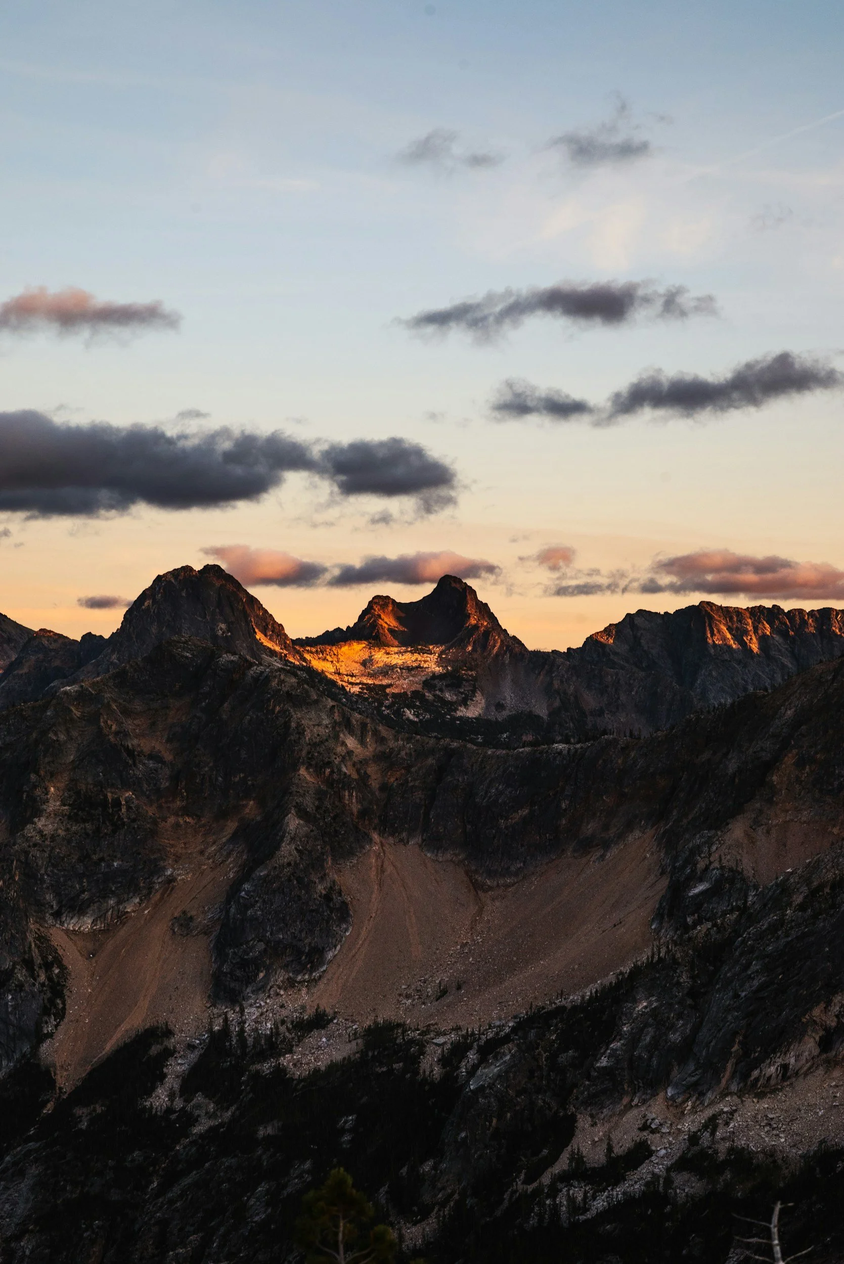 Sunset over rugged mountain peaks with dark clouds overhead.
