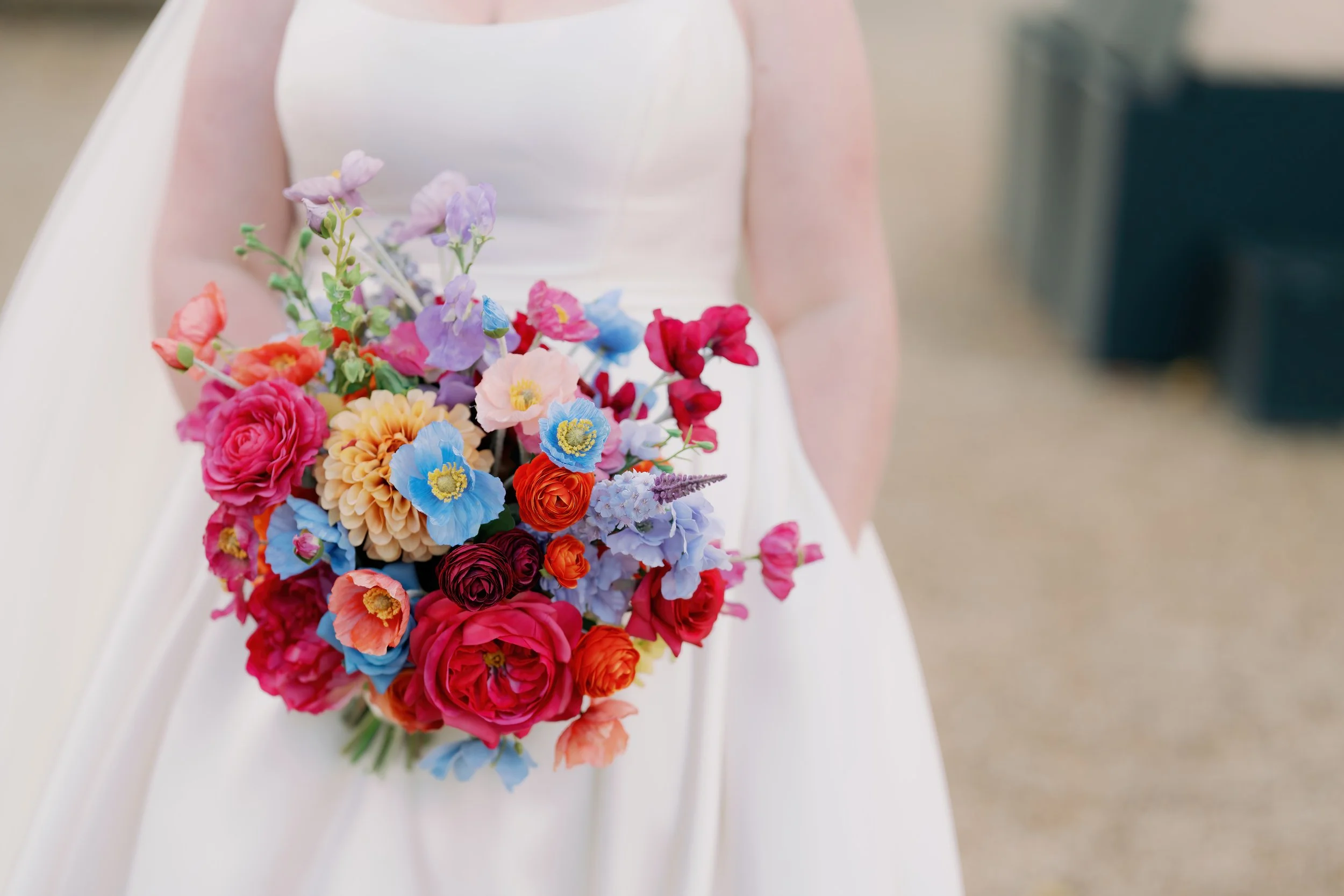 Bridal dress with a colorful bouquet of flowers including roses, poppies, and other mixed flowers.