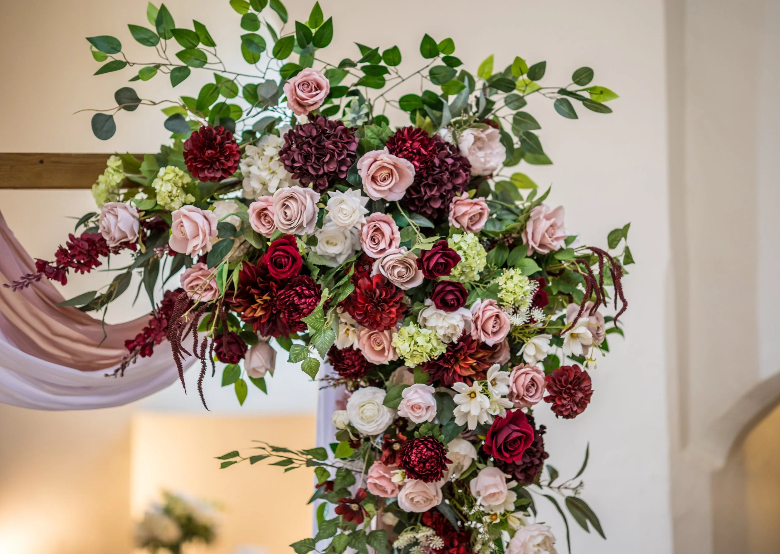 A floral arrangement with roses, hydrangeas, dahlias, and greenery in shades of pink, red, and white, displayed as a decorative centerpiece.