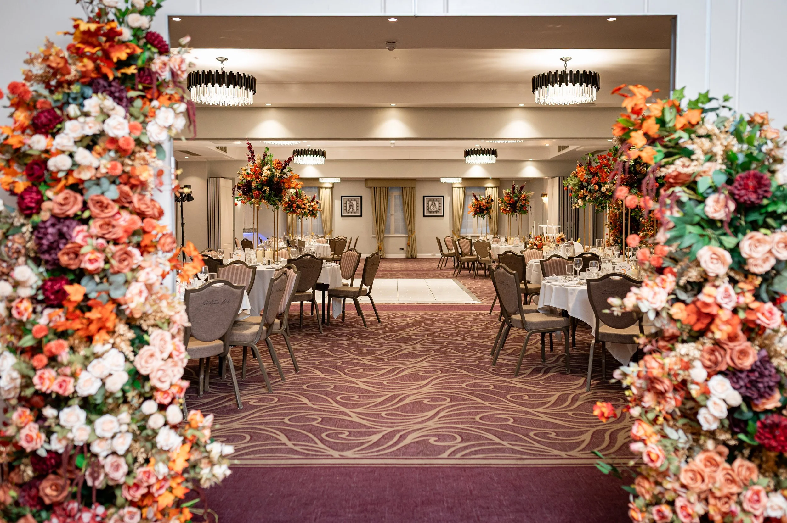 Elegant banquet hall decorated with floral arrangements and set for a formal event, viewed through a floral archway.