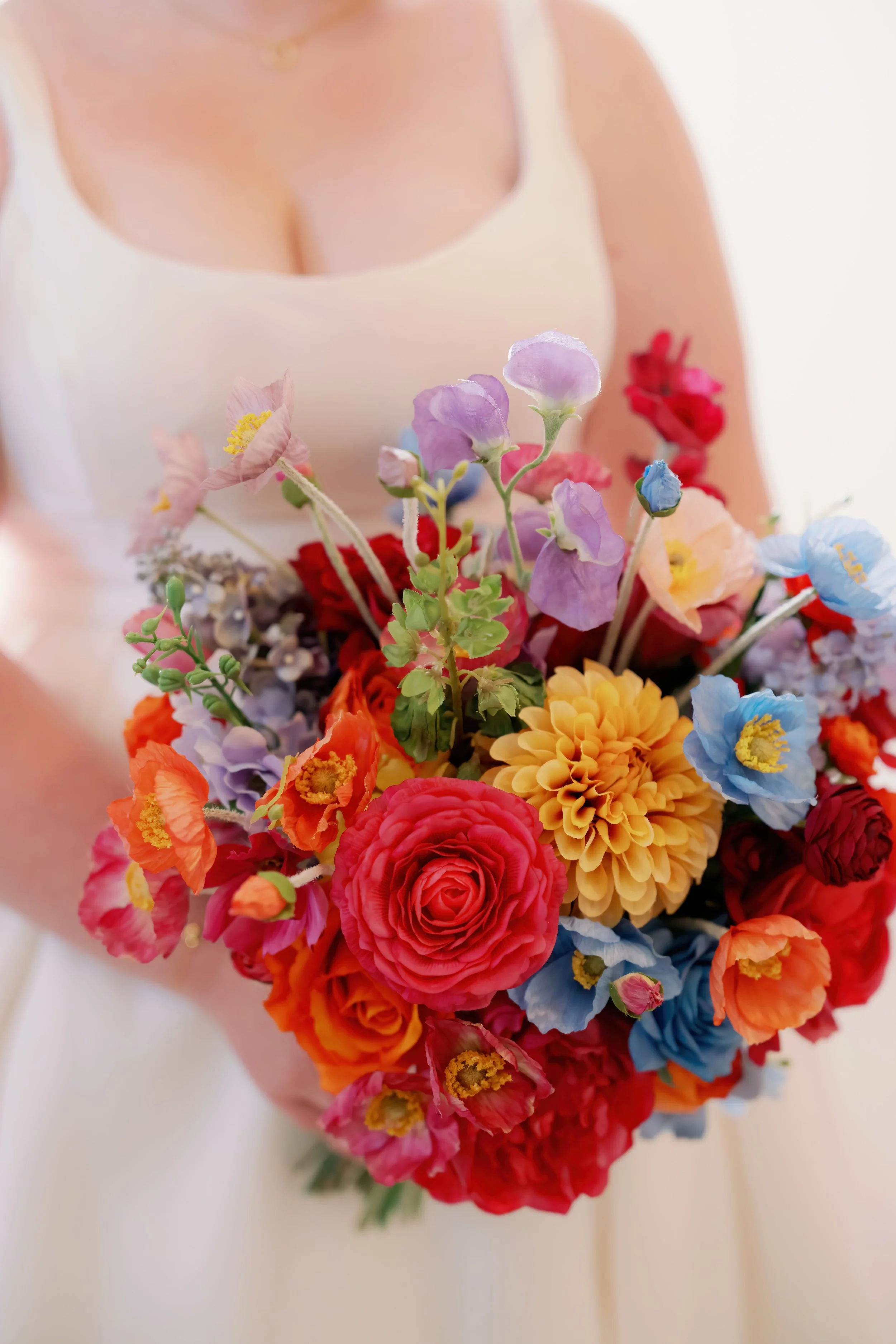 A woman in a white dress holding a colorful bouquet of various flowers.