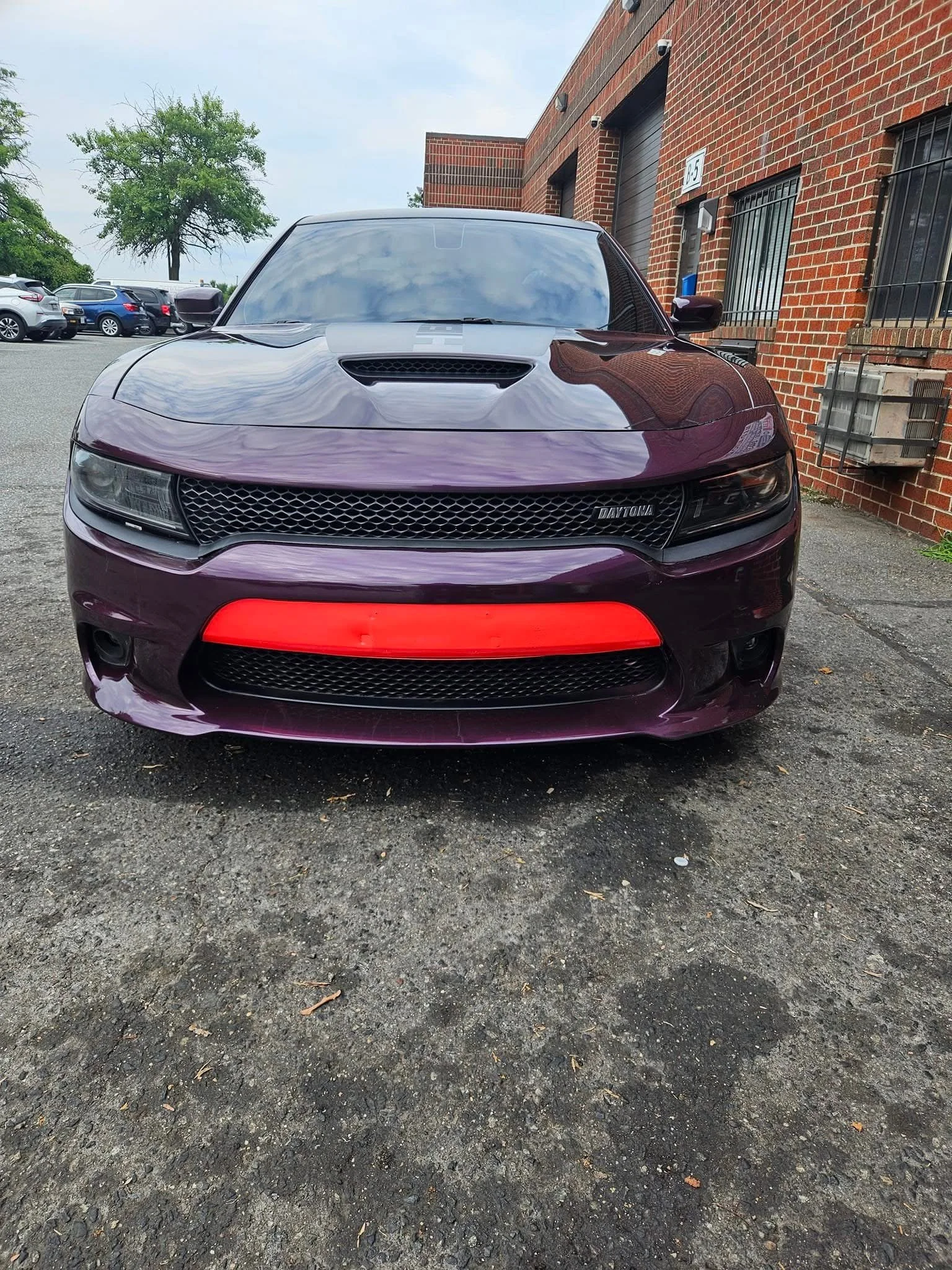 Front view of a purple Dodge Charger Daytona parked in a lot with a red front lip and a brick building in the background.