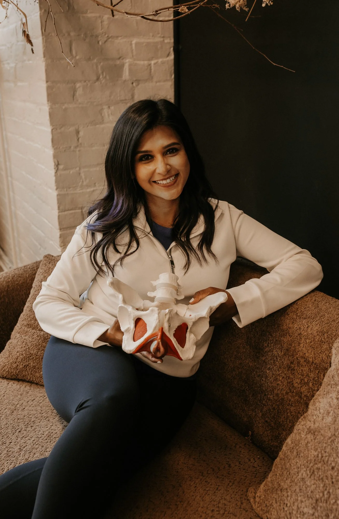Dr. Sheron DSouza smiling at camera holding a pelvis model.