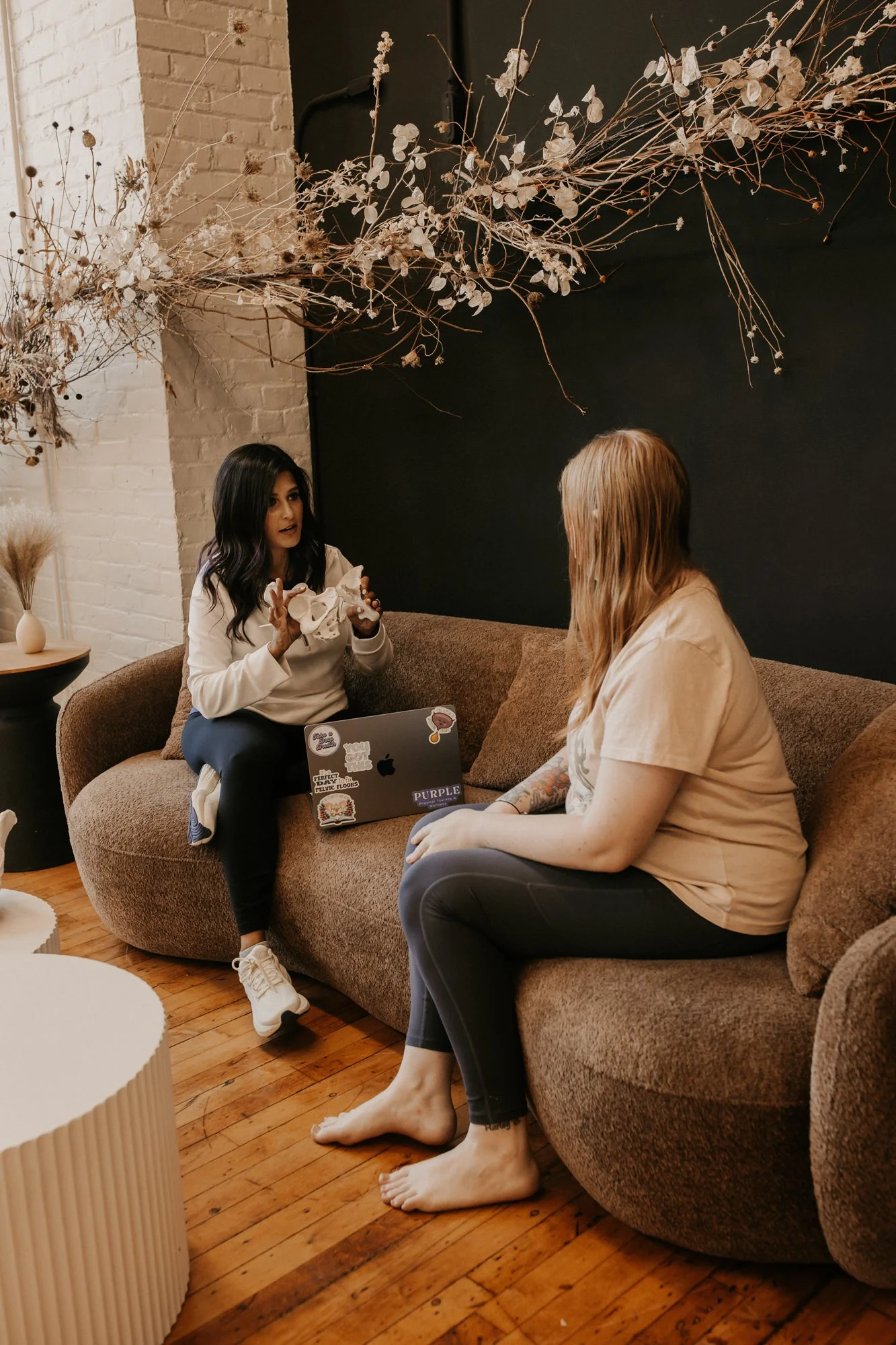 pelvic floor therapist sitting on a couch with a patient holding a pelvis model and talking