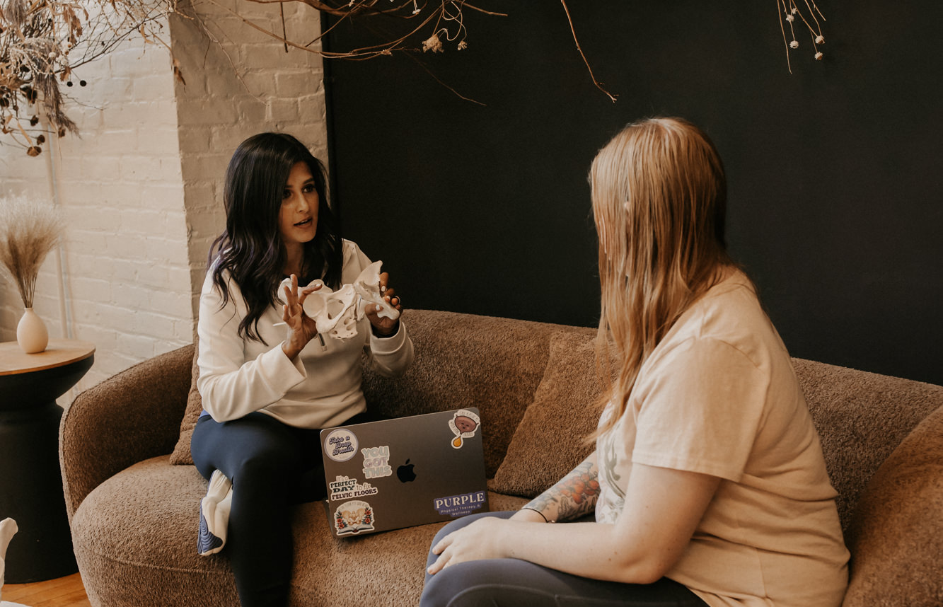 a pelvic therapist talking to a patient while holding a pelvis model