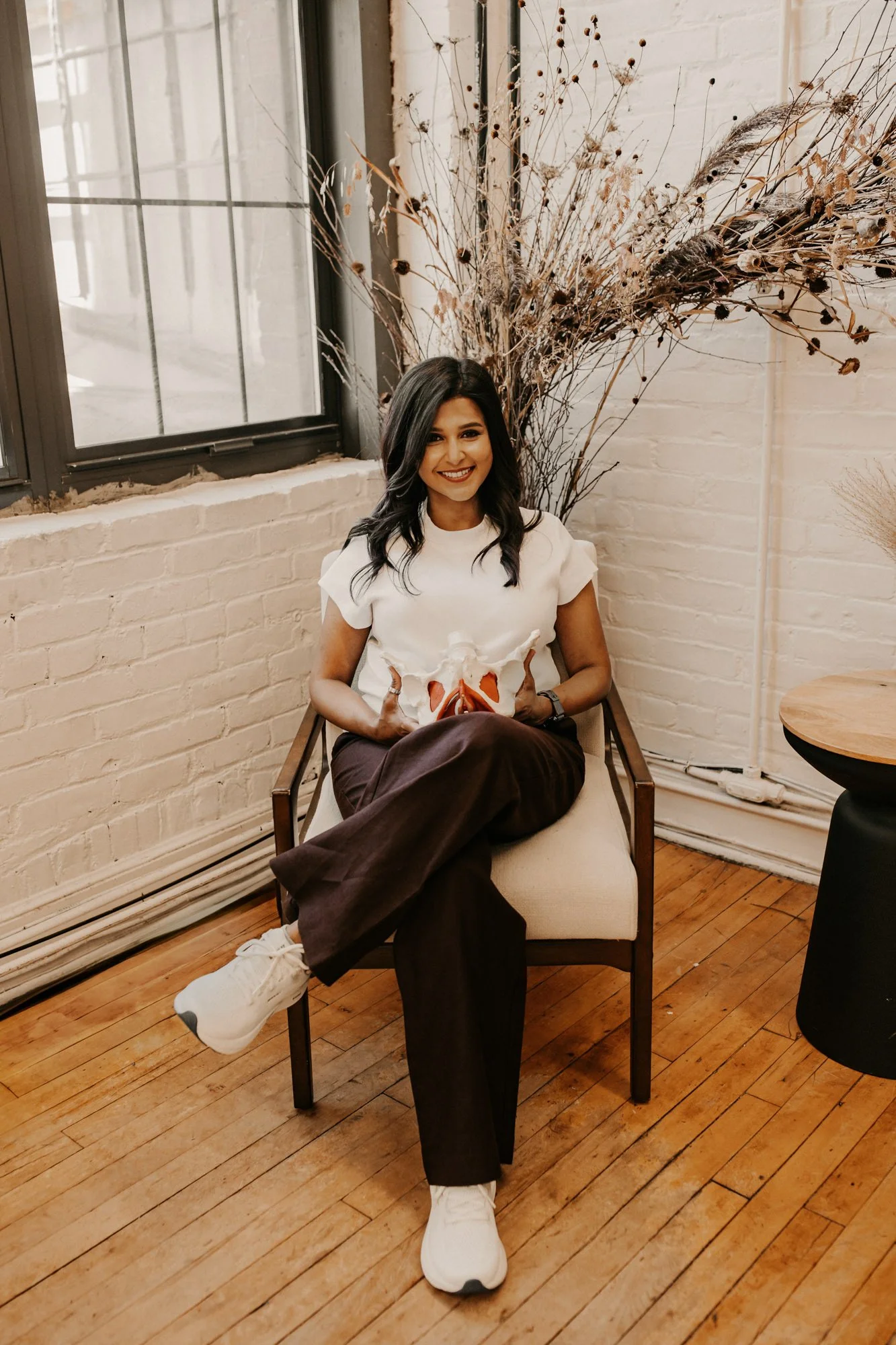 Sheron Dsouza, a pelvic floor therapist, smiling a the camera while holding a pelvis model