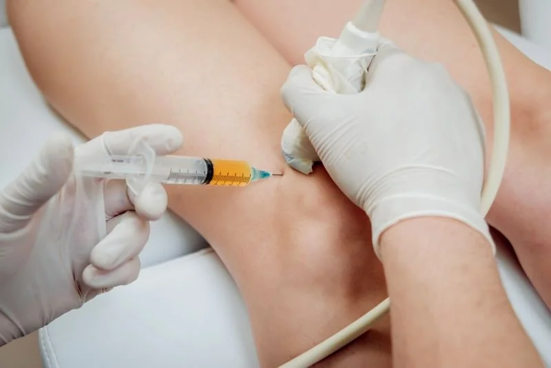 A medical professional in gloves administering an injection into a patient's thigh.