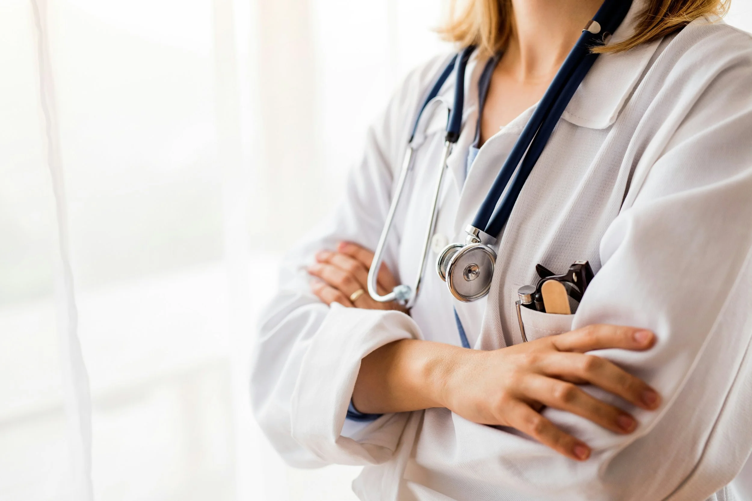 Medical professional with arms crossed, wearing a white coat and stethoscope.