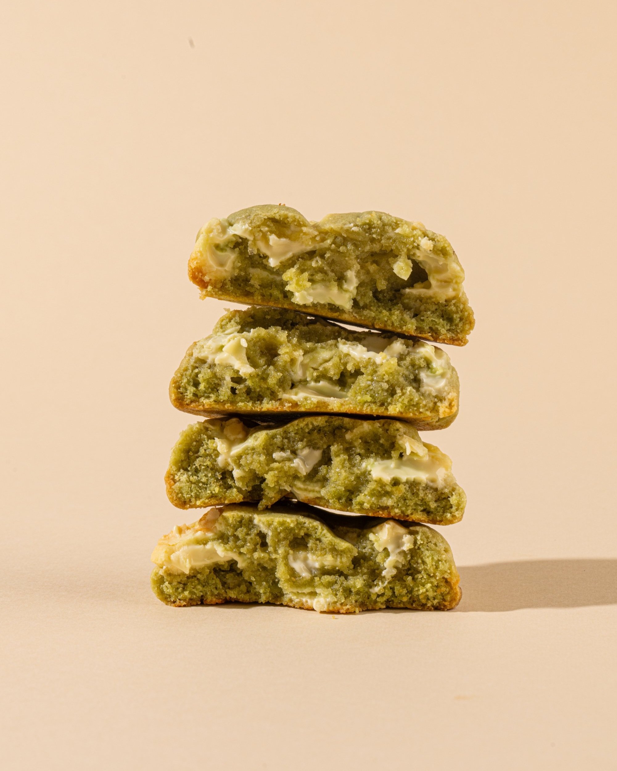 Four stacked green cookies with white chocolate chips on a light beige background.