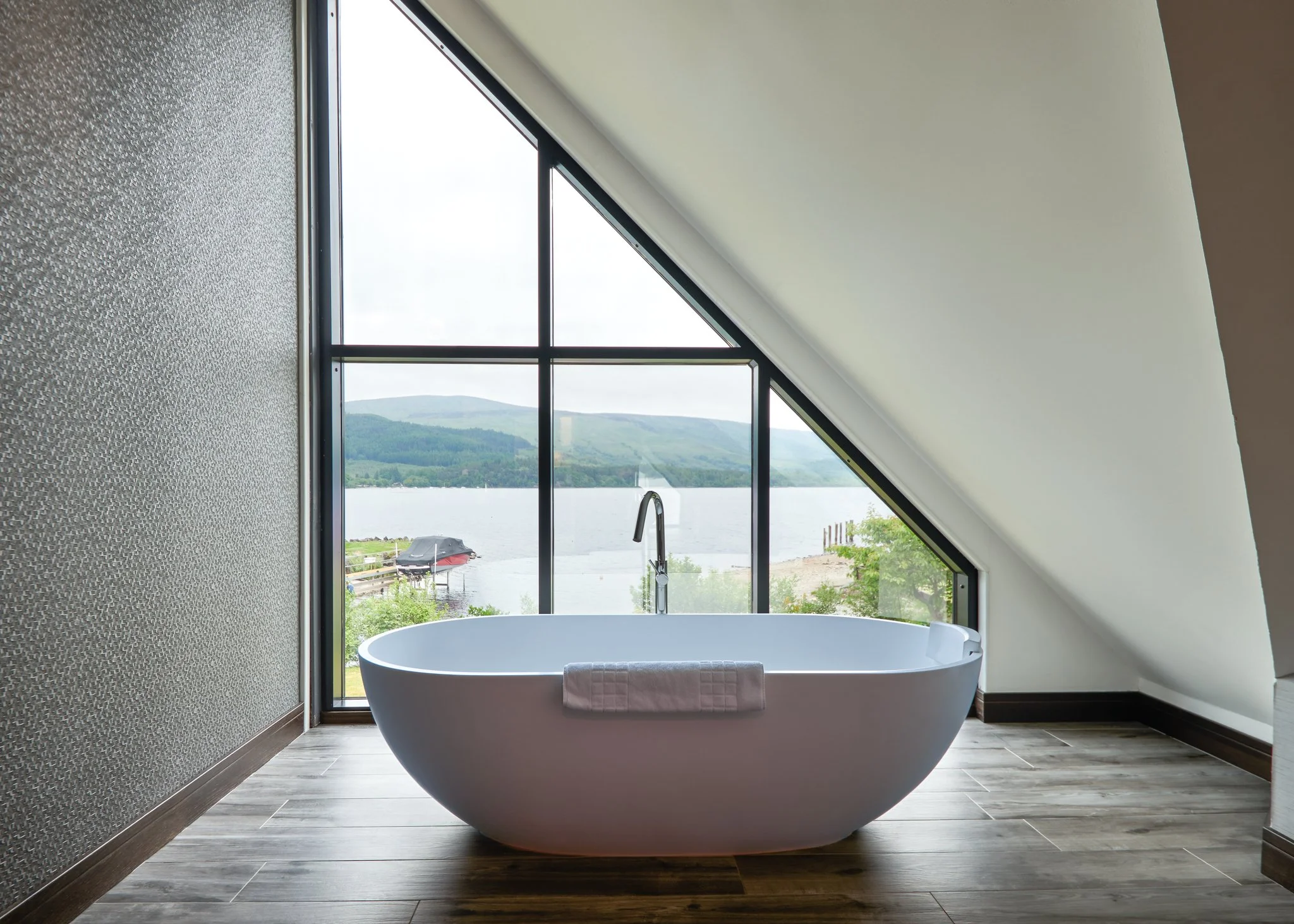Freestanding bathtub by large window with panoramic lake view in modern bathroom interior