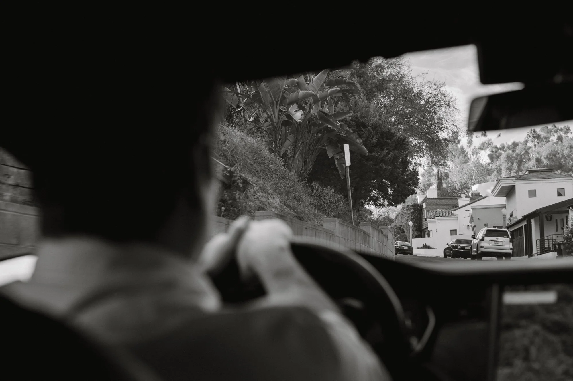 Black and white photo of a man driving a car, view through the windshield.