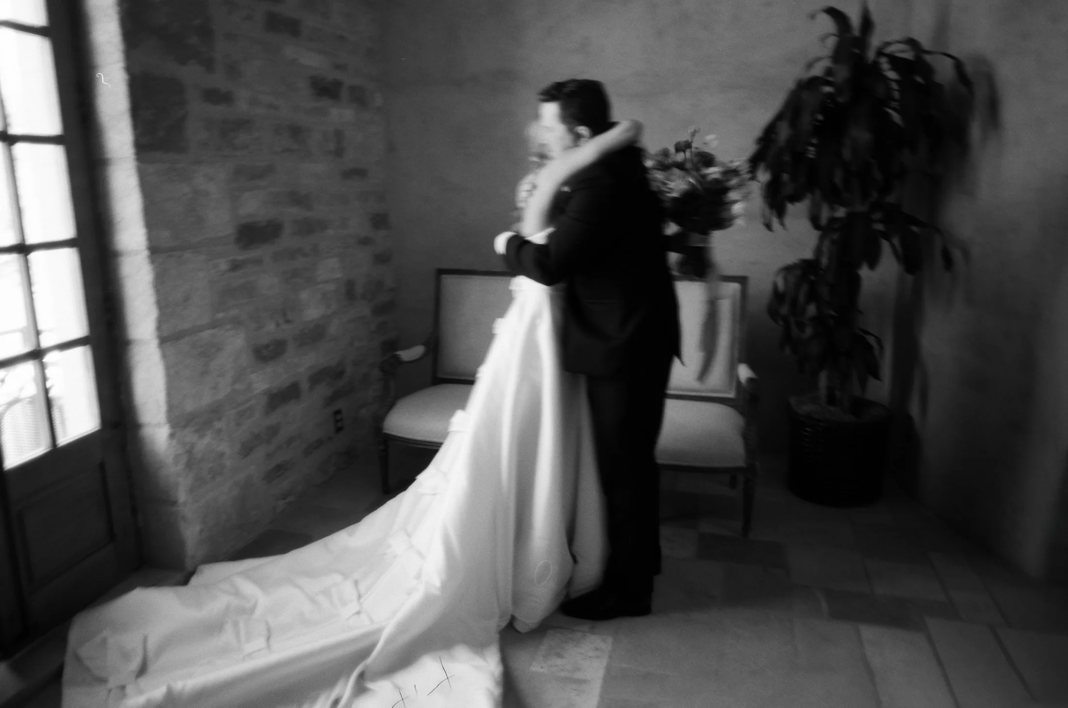 Black and white photo of bride and groom embracing in a stone hallway.