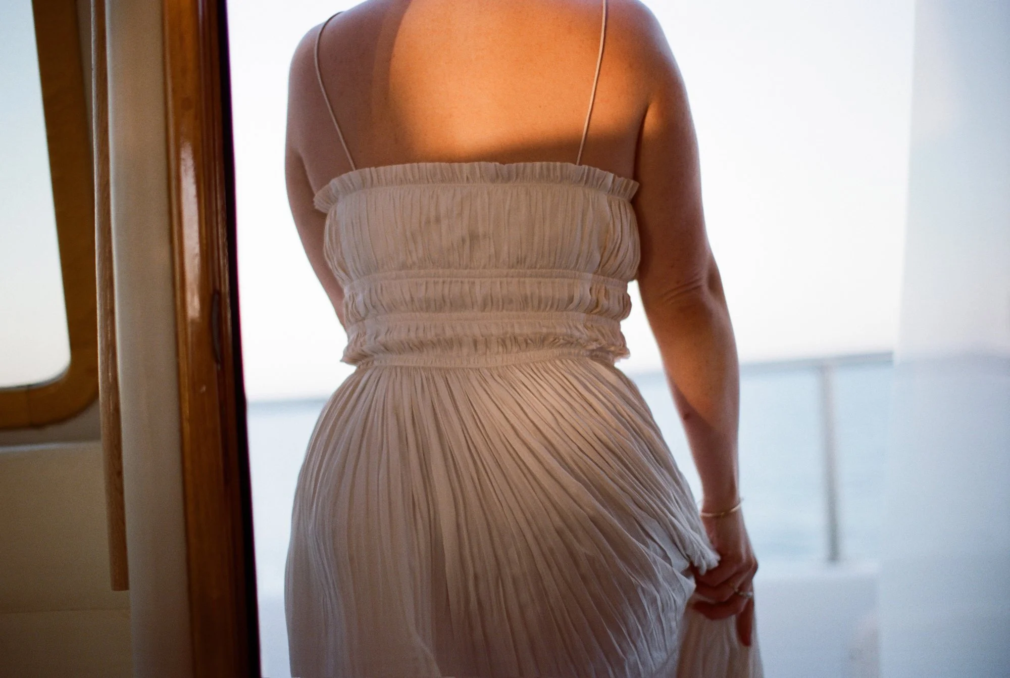 Bride in a fitted dress, standing by the yacht’s window.